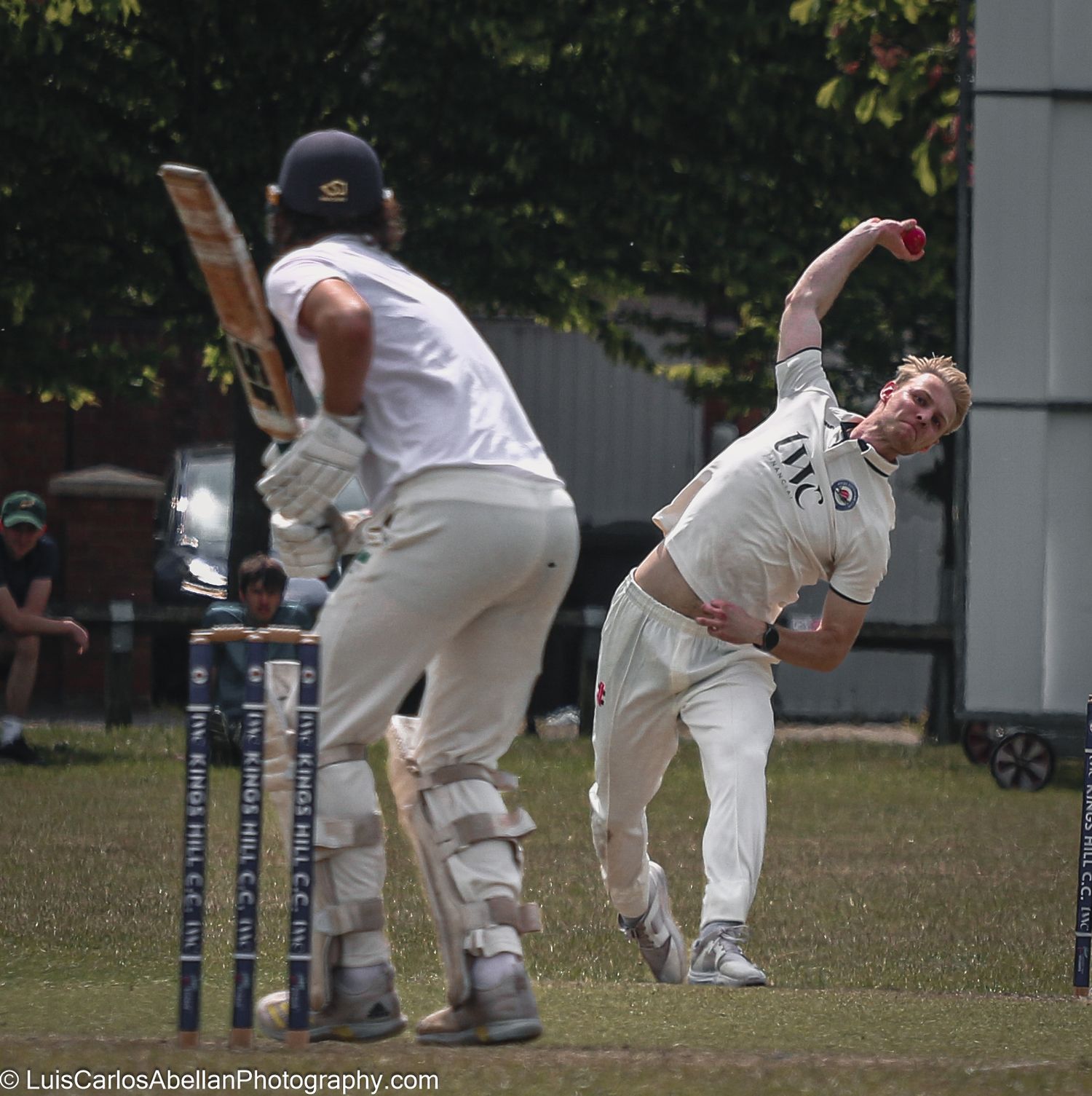 A bowler in a white kit delivers a red cricket ball during a match at Kings Hill Cricket Club, photographed by Luis Carlos Abellan in Kent.