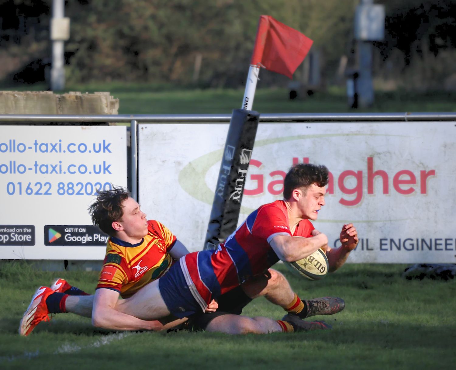 A rugby player in a red and blue kit diving to score a try as he is tackled, shot by Luis Carlos Abellan Photography in Aylesford