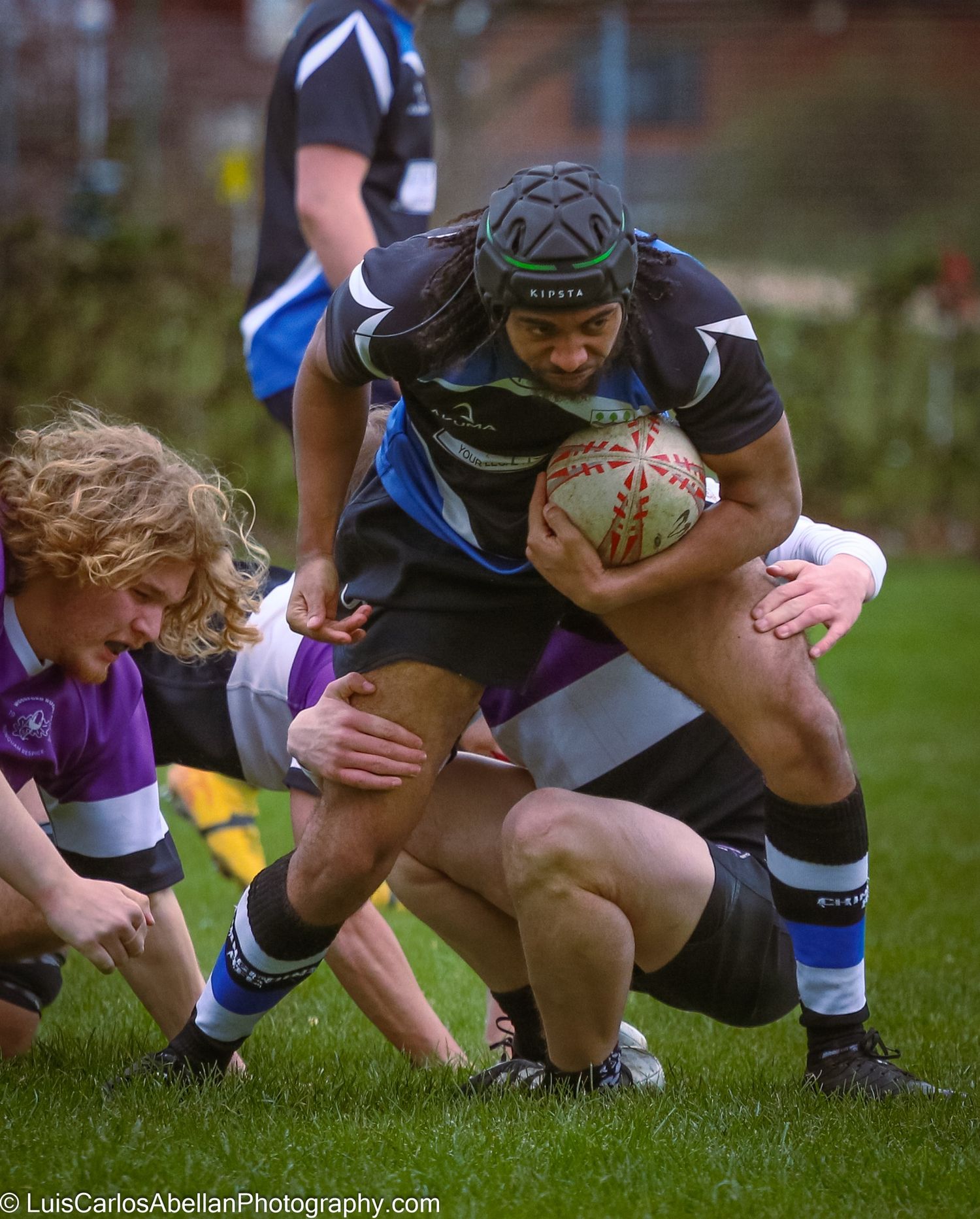 A rugby player wearing a scrum cap charges forward with the ball during a competitive game, photographed by Luis Carlos Abellan in Kent.