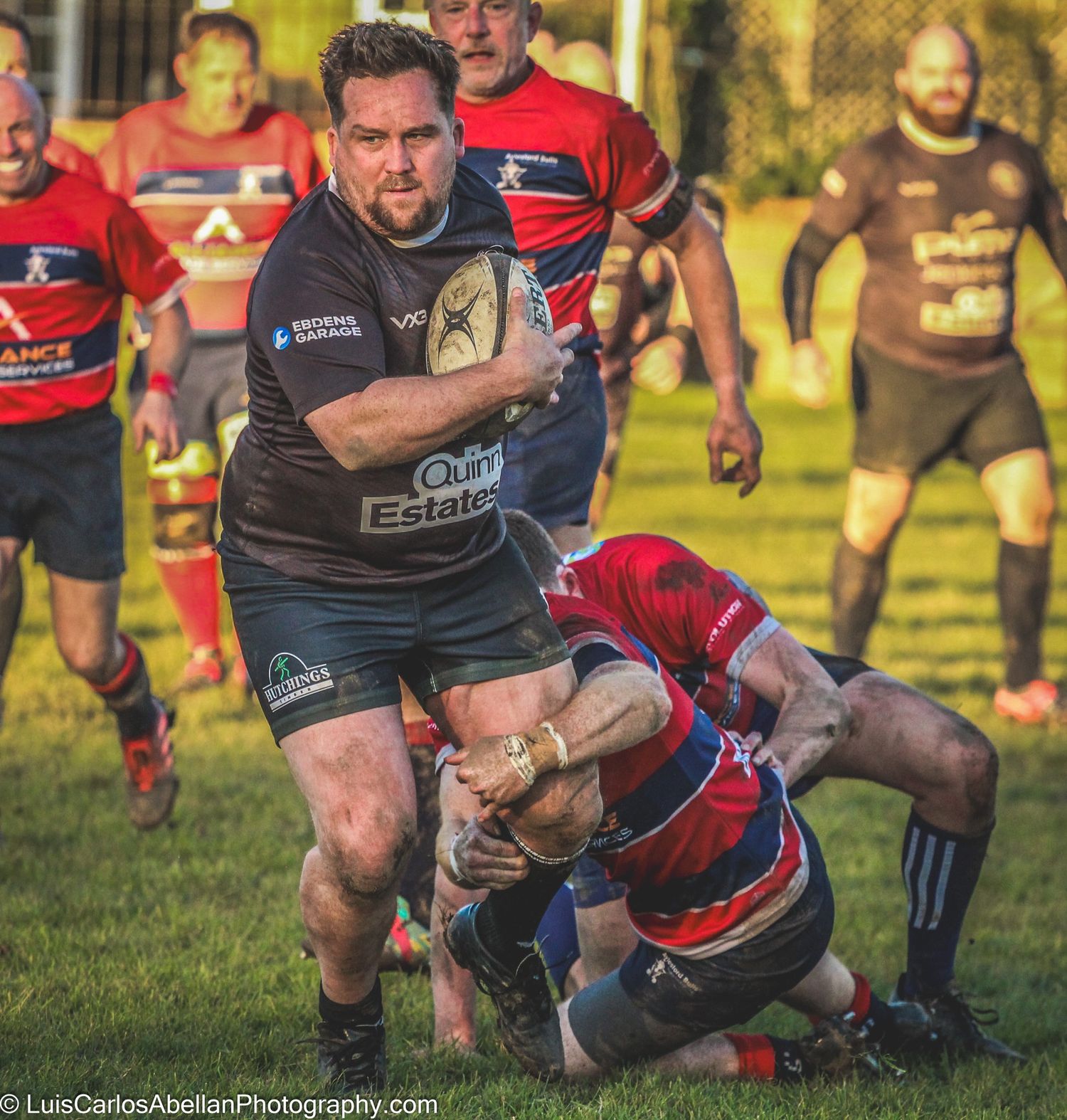 Rugby player in a black kit powering through a tackle during a hard-fought match in Kent. Sports photography by Luis Carlos Abellan.