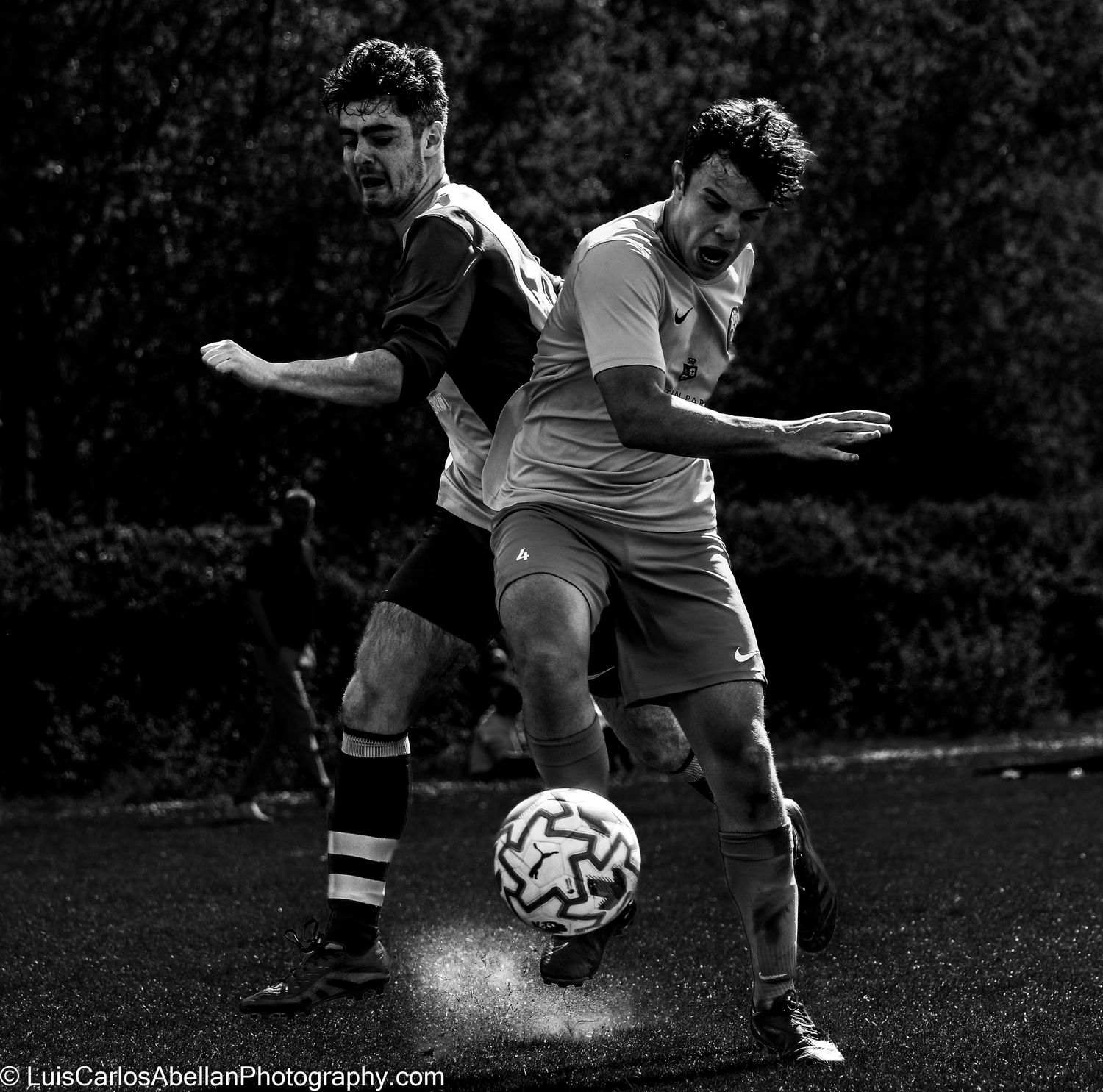 Close-up black and white action shot: two footballers in South East England competing for the ball on a pitch. Captured by Luis Carlos Abell