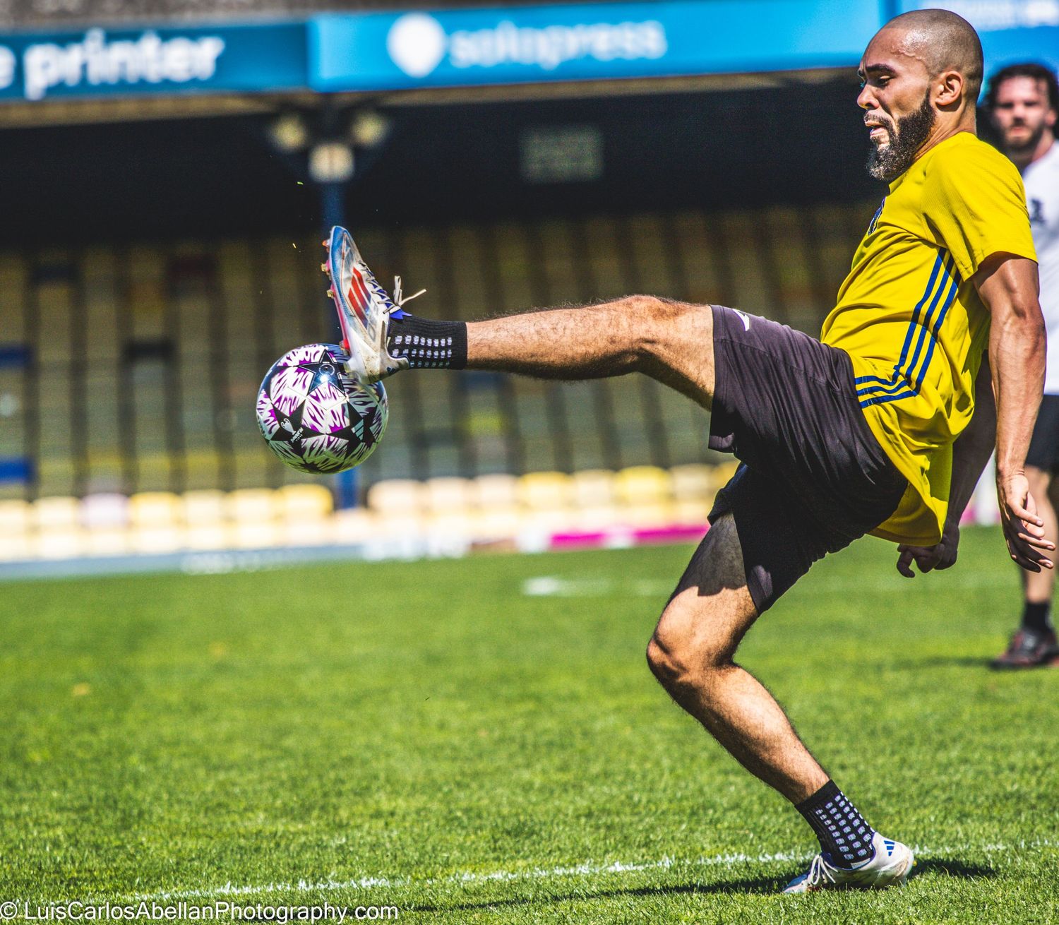 Action shot of an amateur football player in a yellow and black kit dynamically controlling a football with his foot during a local match