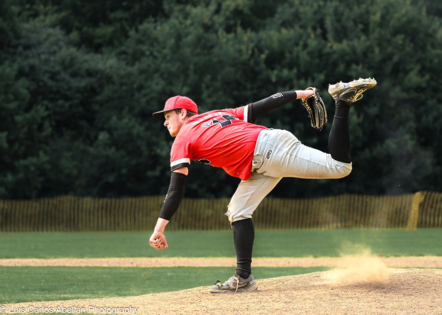 A baseball pitcher in a red jersey and cap mid-throw on the mound, captured by Luis Carlos Abellan Photography in Kent.