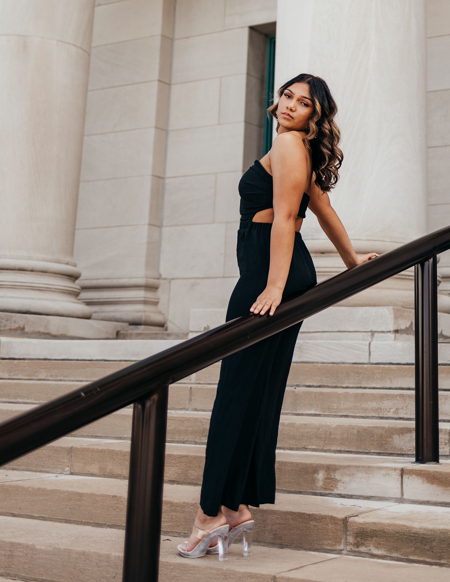 High school senior is elegant black dress on the steps of the art museum in St. Louis, MO.