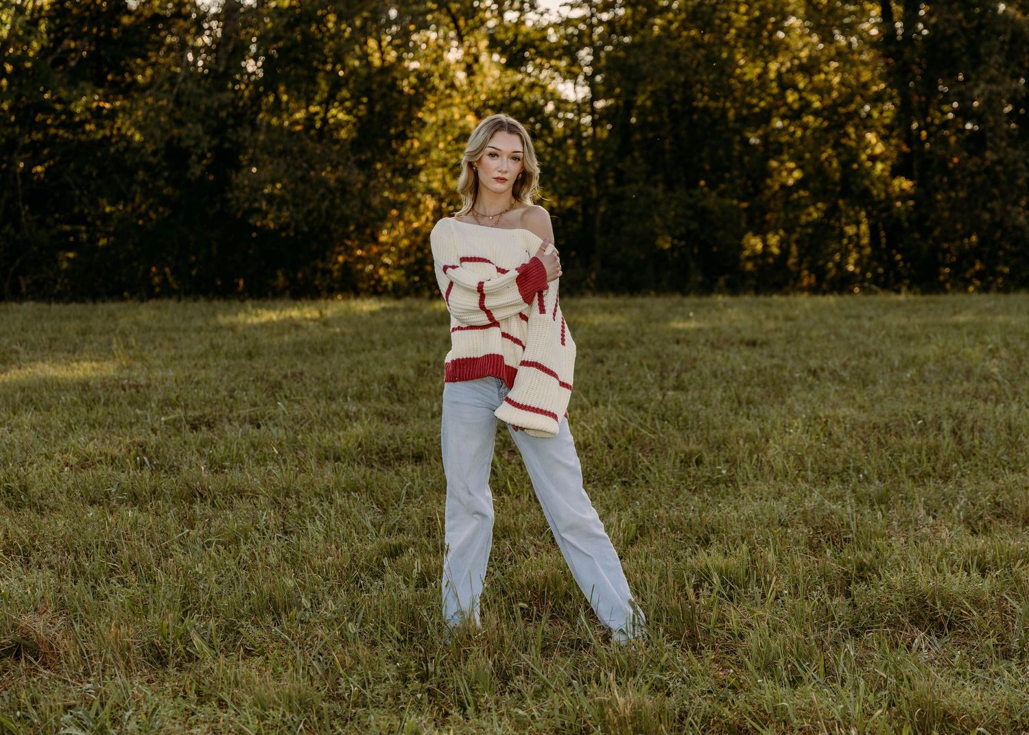 High school senior in a red and white striped sweater and light denim in a senior photo session in a field in St. Robert, MO.