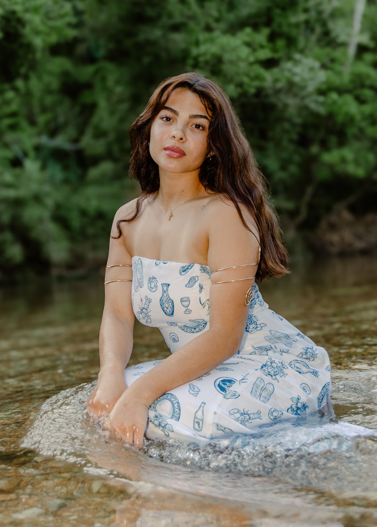 High school senior in a white floral pattern dress in the creek for senior pictures in Waynesville, MO.