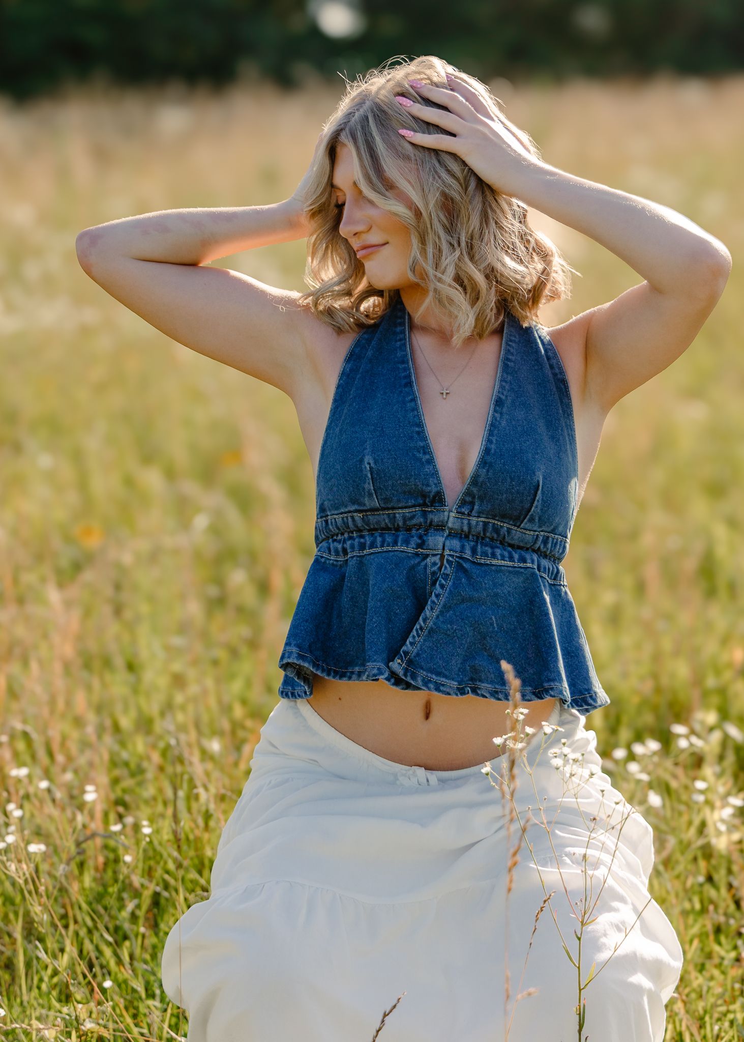 High school senior in a denim halter top and flowy white skirt in a field in Ft. Leonard wood, MO. Senior photos