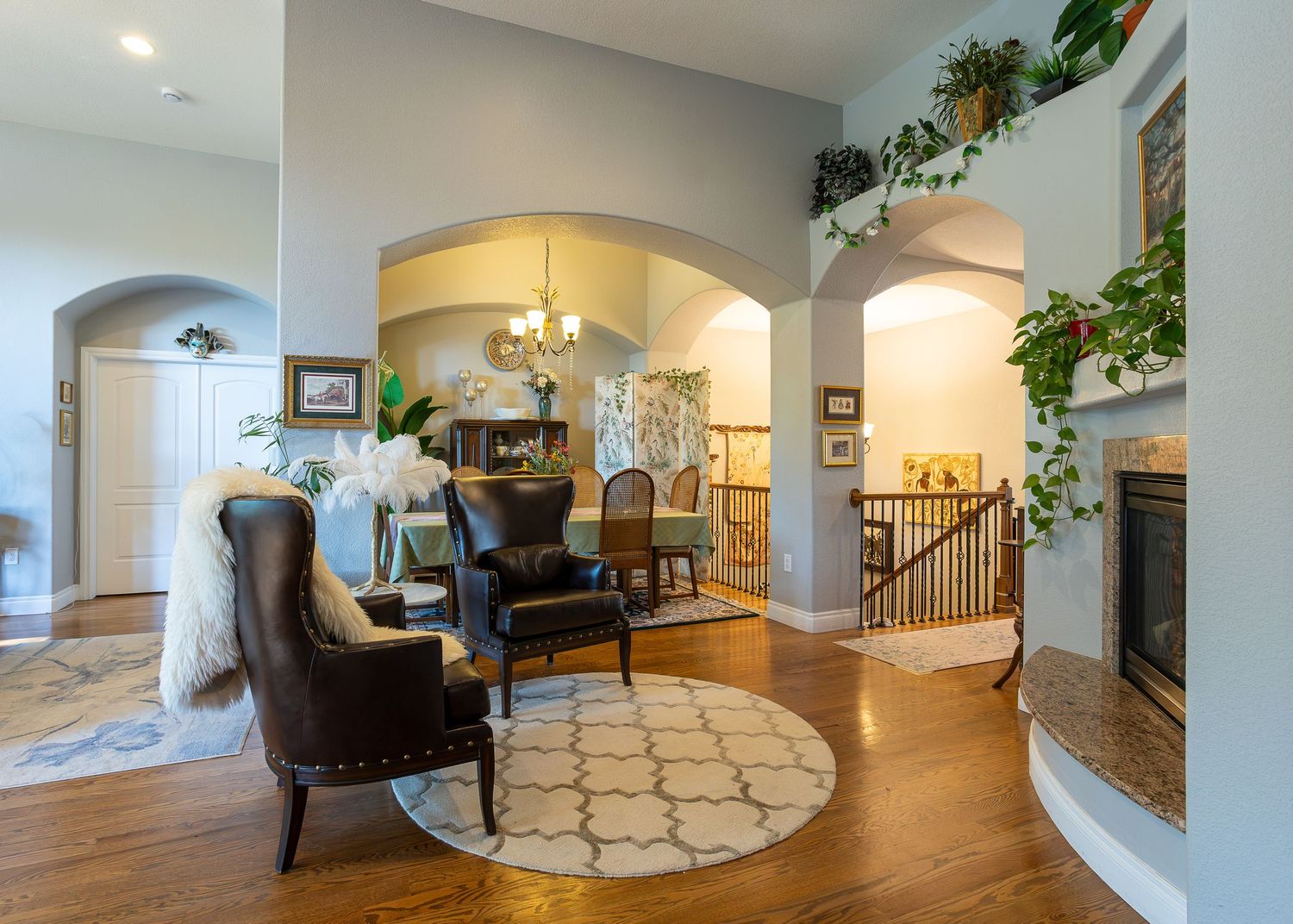 Elegant living room with hardwood floors, arched doorways, leather chairs, a round rug, fireplace, and lush greenery accents.
