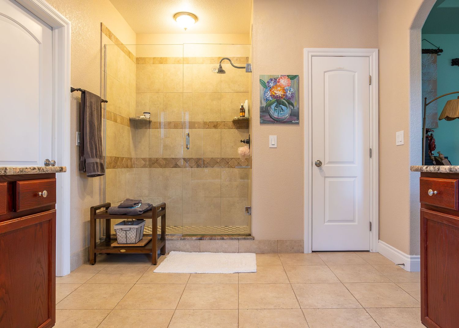 Spacious master bathroom with walk-in tiled shower, wooden bench, dual vanities, and elegant arched doorway.