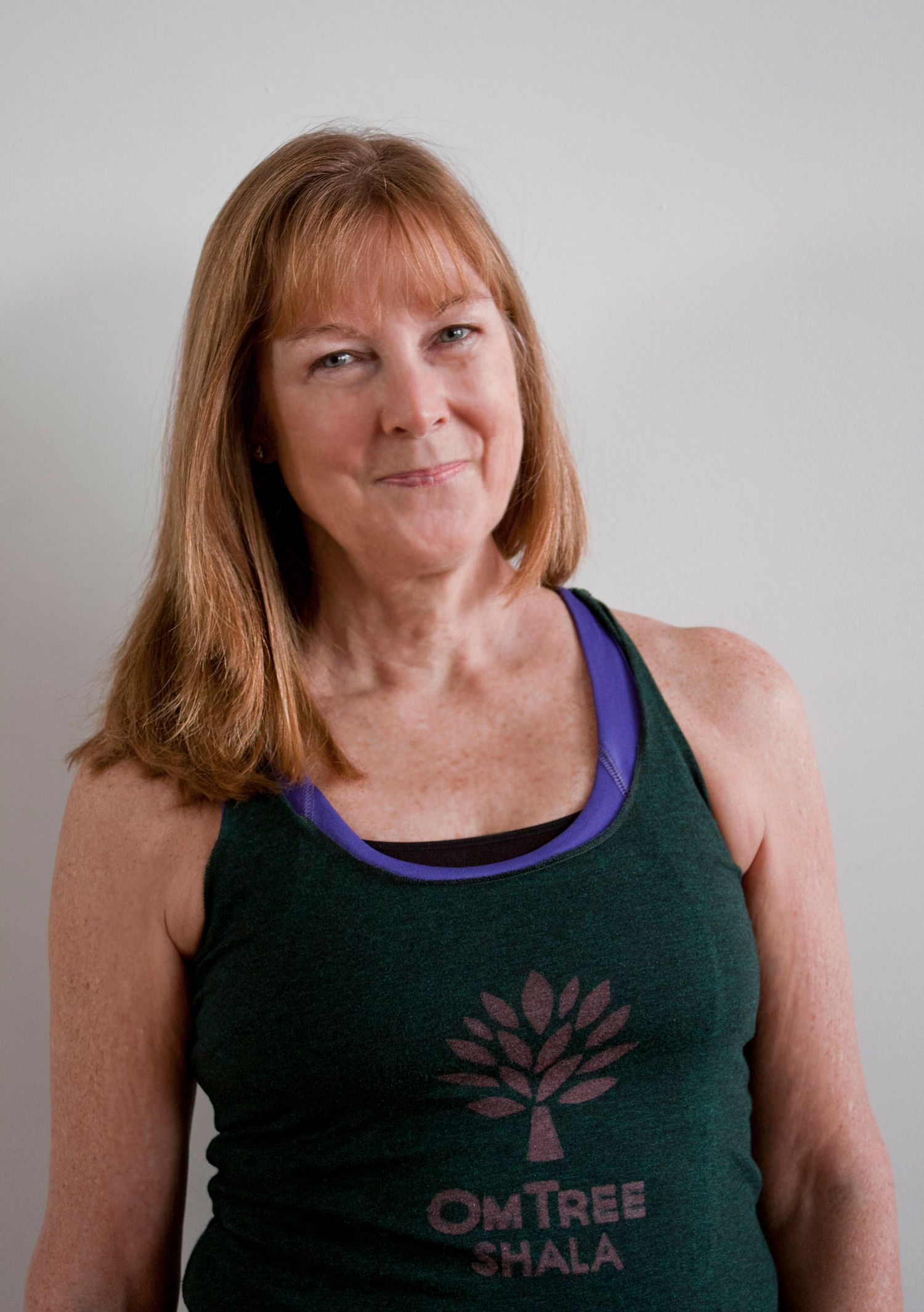Smiling older woman with red hair wearing green OmTree Shala tank top portrait photo.