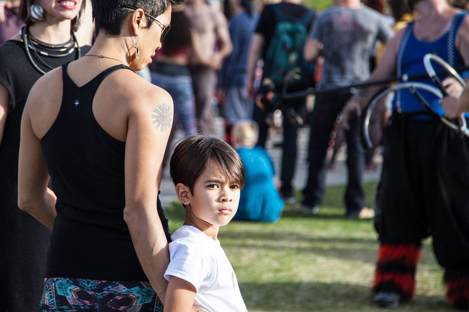 A young boy in a white shirt looks back at a crowd during an outdoor festival event.