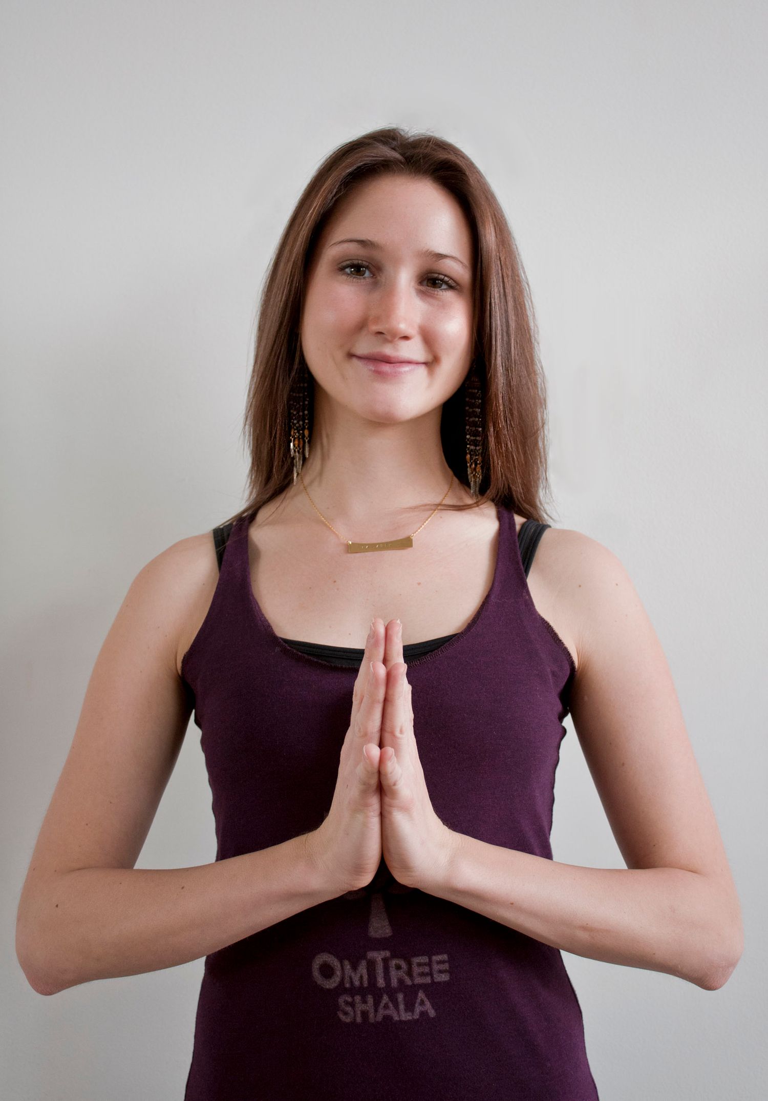 Young woman in purple OmTree Shala tank top performing namaste prayer pose hands gesture.