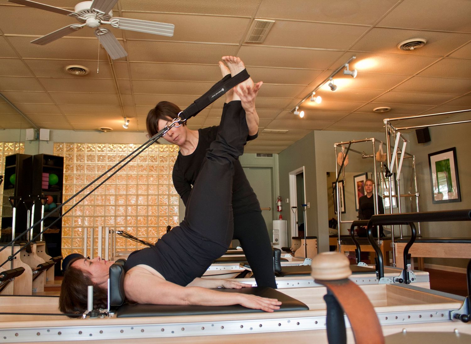 Pilates instructor assisting a client with resistance band exercises on a reformer in a professional studio.
