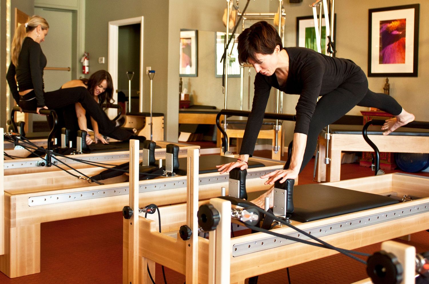Woman performing Pilates exercises on a wooden reformer machine in a professional fitness studio.