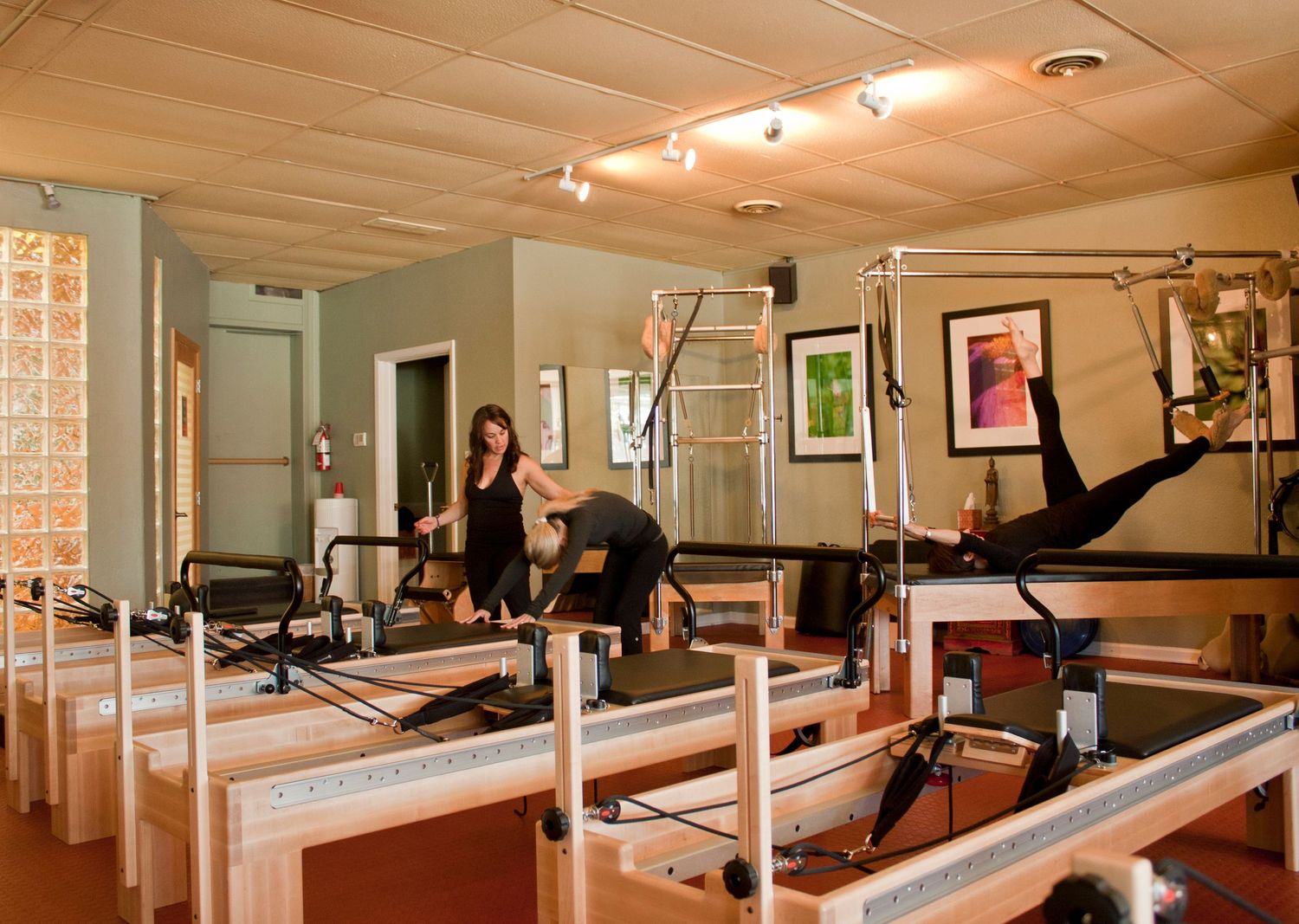 Multiple clients exercising on Pilates reformer machines in a well-equipped professional Pilates studio.