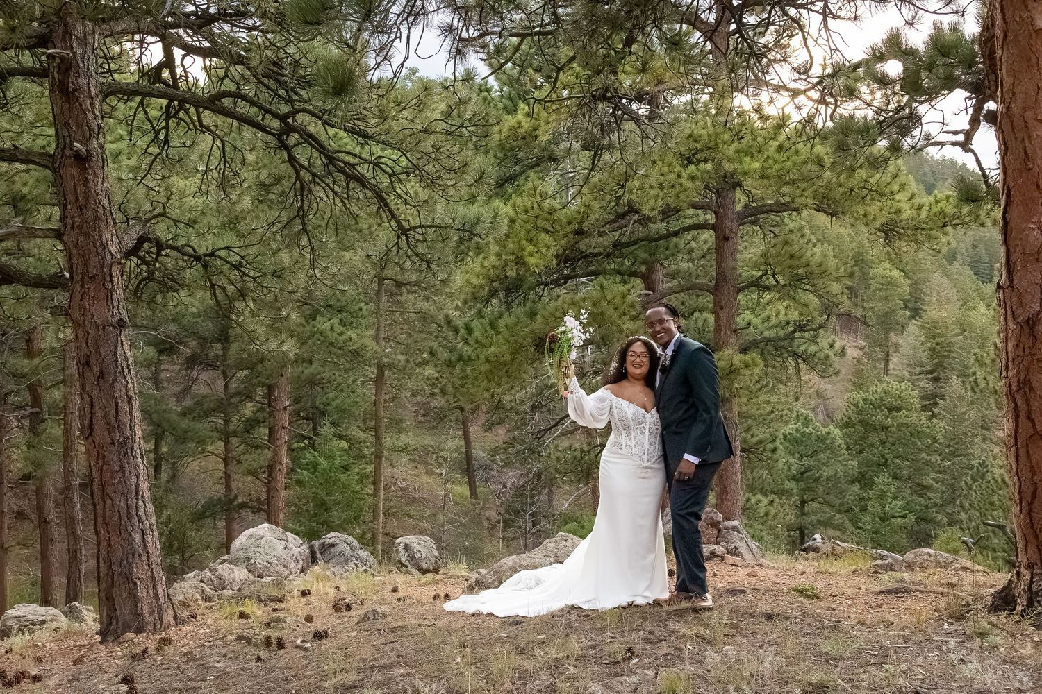 Bride and groom pose together in a pine forest, wearing wedding attire, celebrating their outdoor mountain wedding.