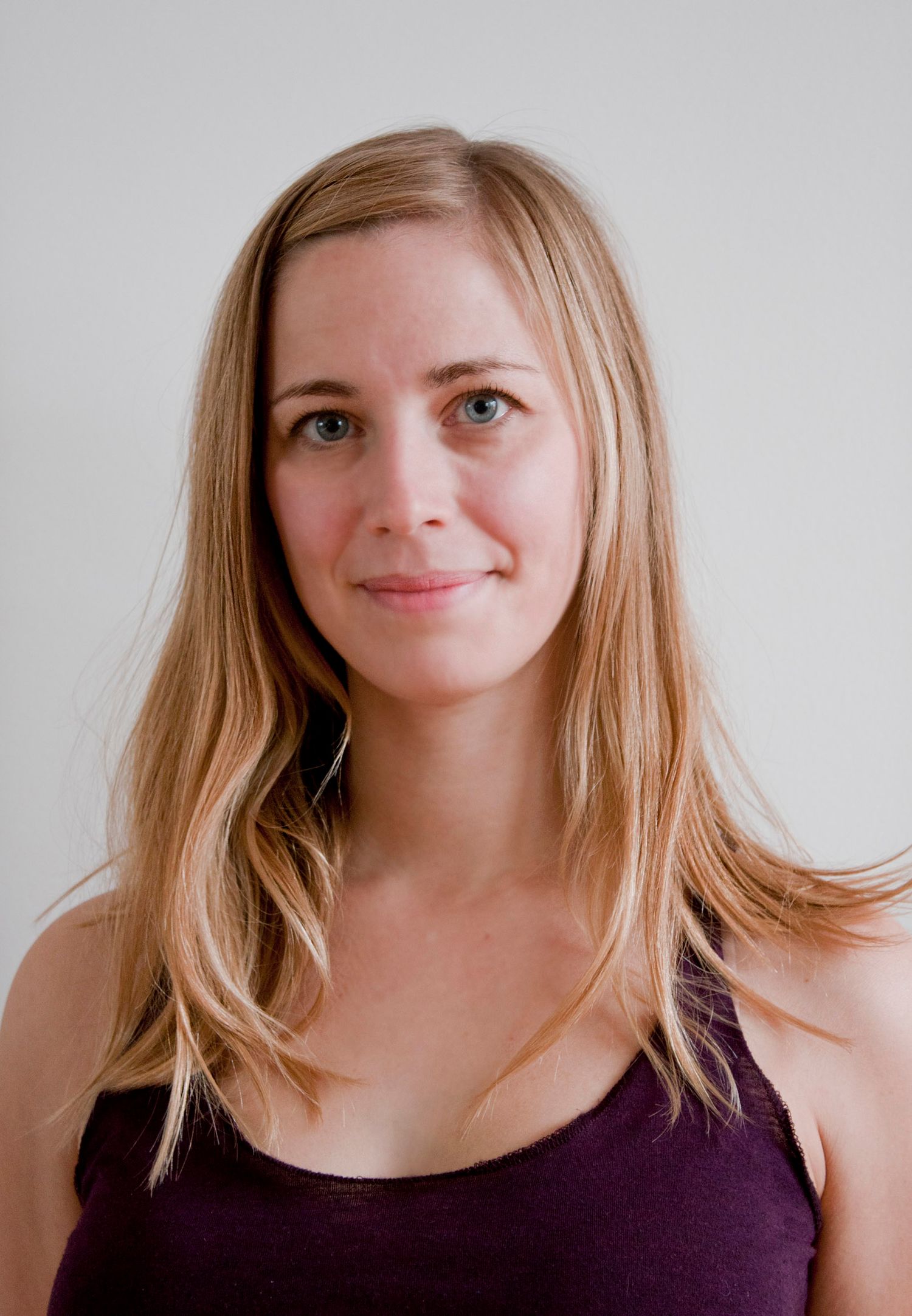 Portrait of blonde woman with blue eyes wearing purple tank top against white background.