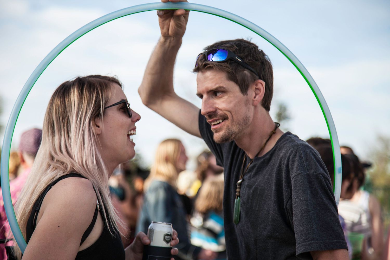 A smiling couple talking closely at an outdoor festival with a hula hoop overhead.