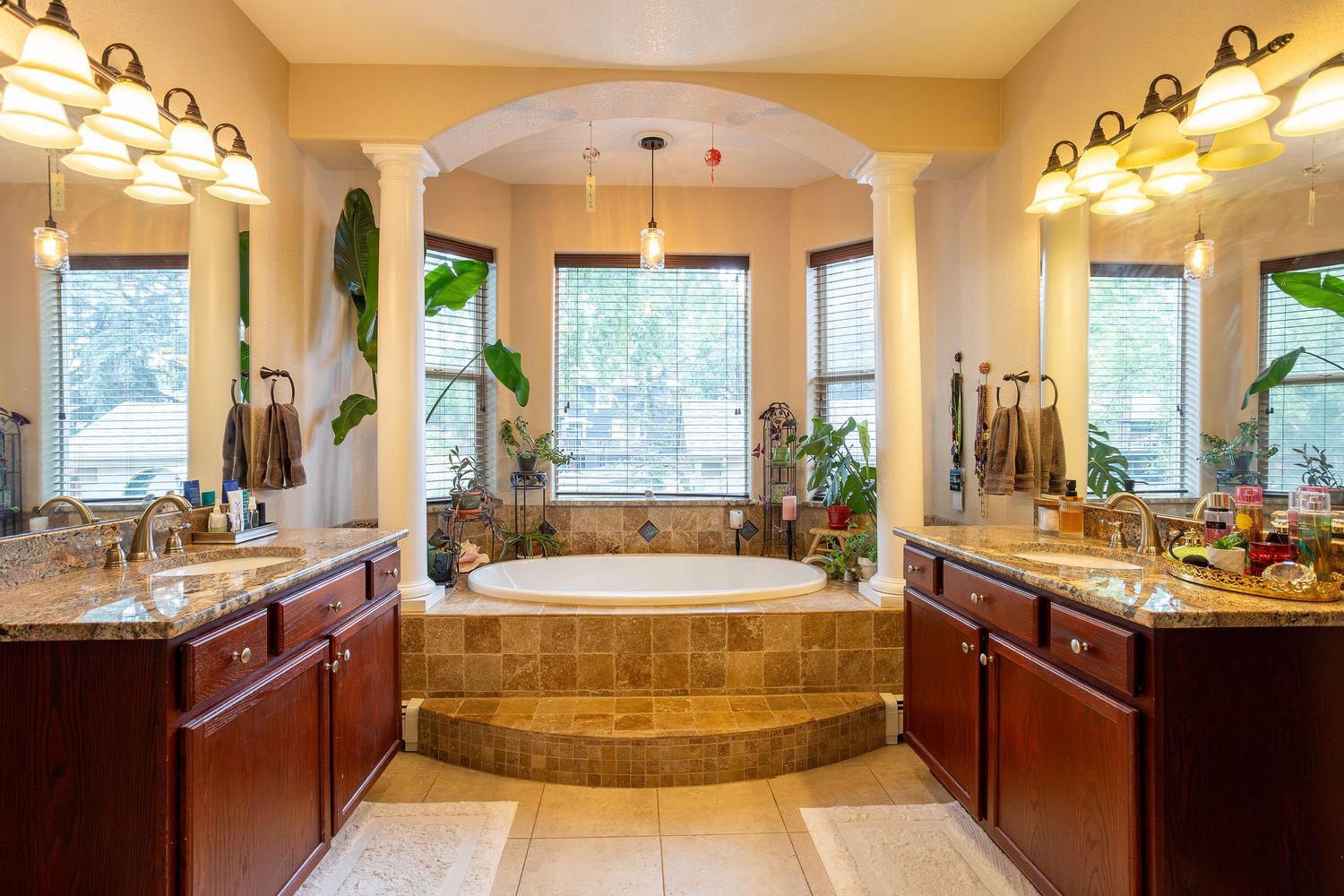Luxurious master bathroom with dual cherry wood vanities, large soaking tub, arched columns, and elegant lighting fixtures.