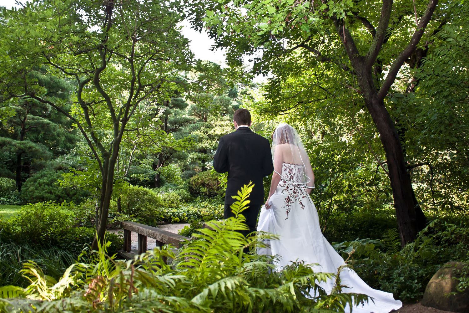 Bride and groom walking hand in hand through a lush green garden on their wedding day.