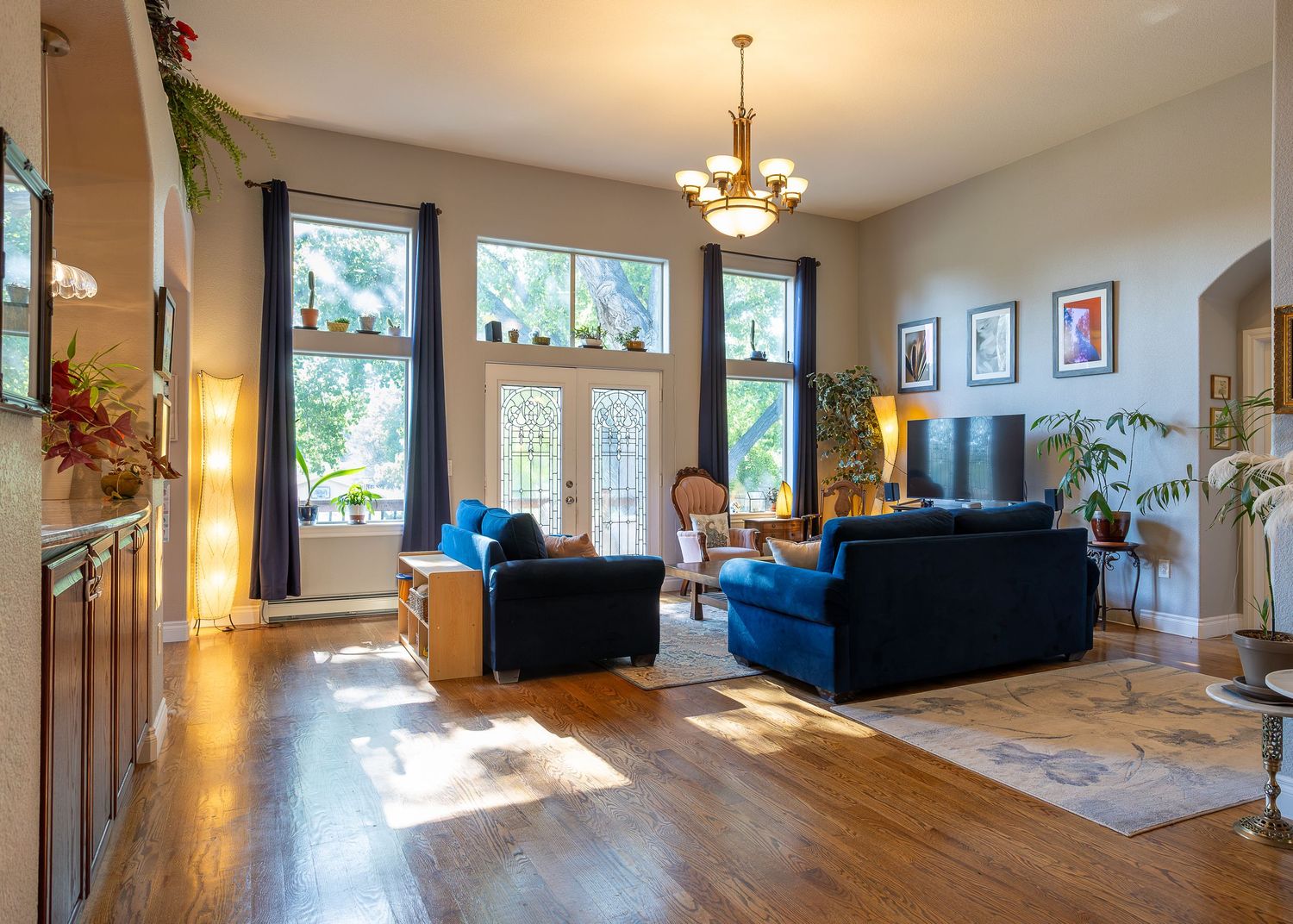 Bright living room with hardwood floors, blue sofas, large windows, and a chandelier in an elegant home.