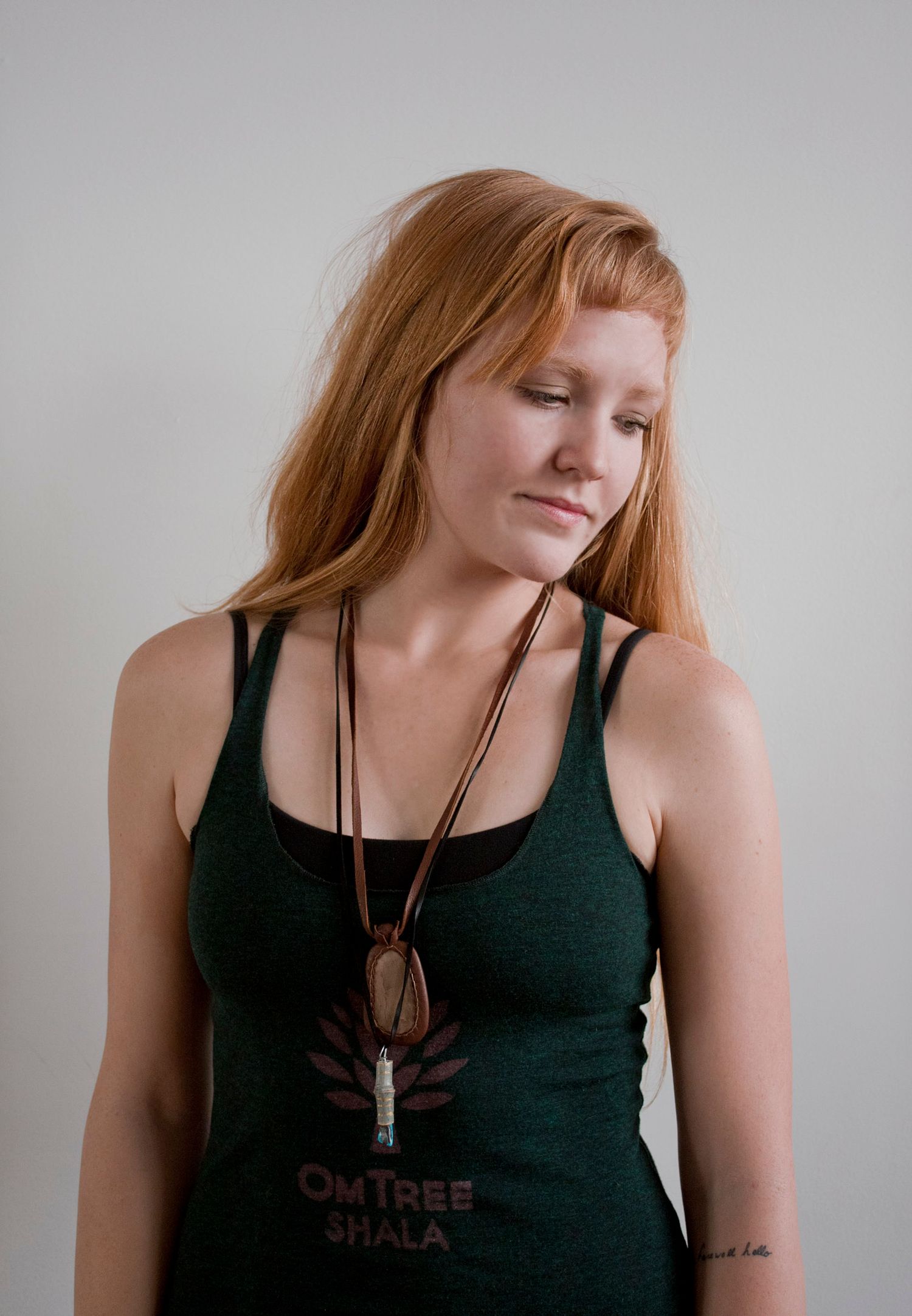 Woman with red hair wearing OmTree Mala green tank top with pendant necklace on white background.