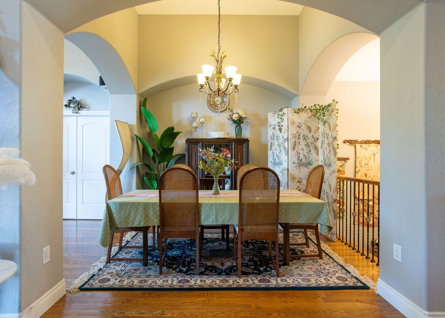 Elegant dining room with arched doorways, chandelier, rattan chairs, and hardwood floors on a decorative area rug.