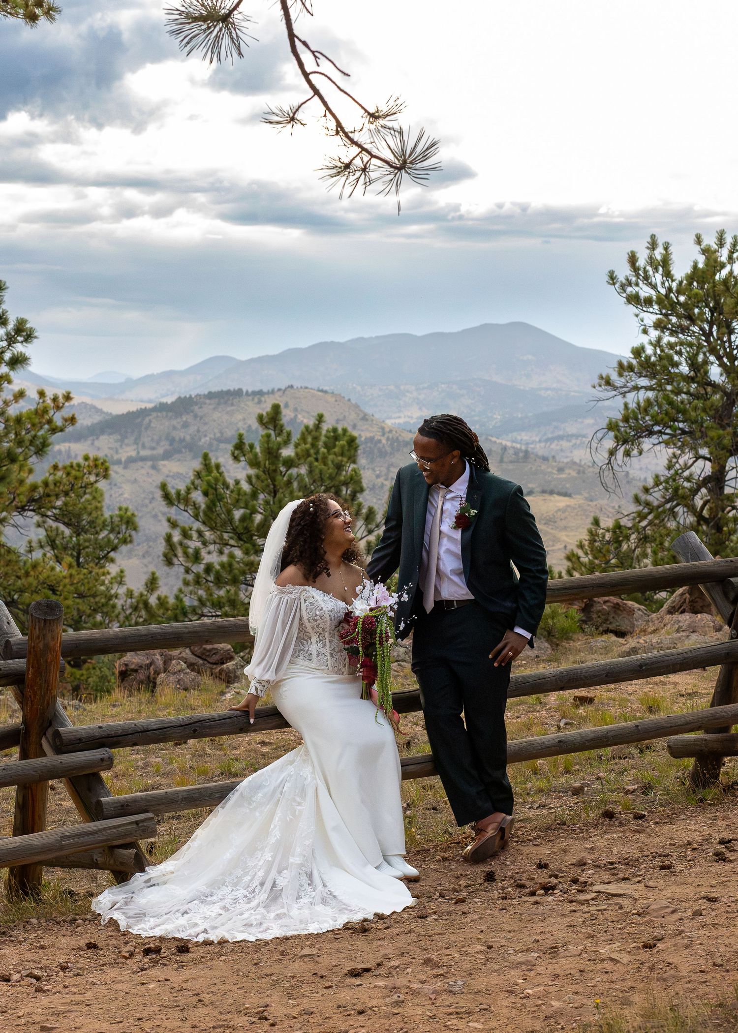 Bride and groom share a romantic moment by a wooden fence with stunning mountain views behind them.
