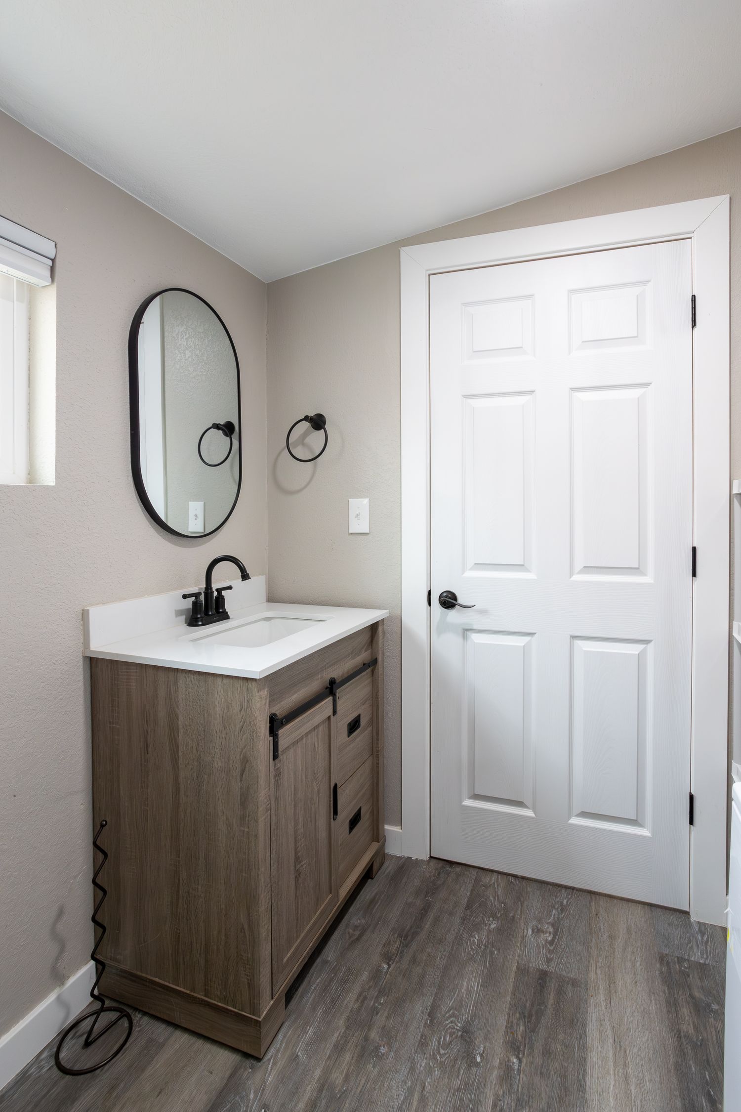Modern bathroom vanity with wood cabinet, white countertop, oval mirror, and six-panel white door.