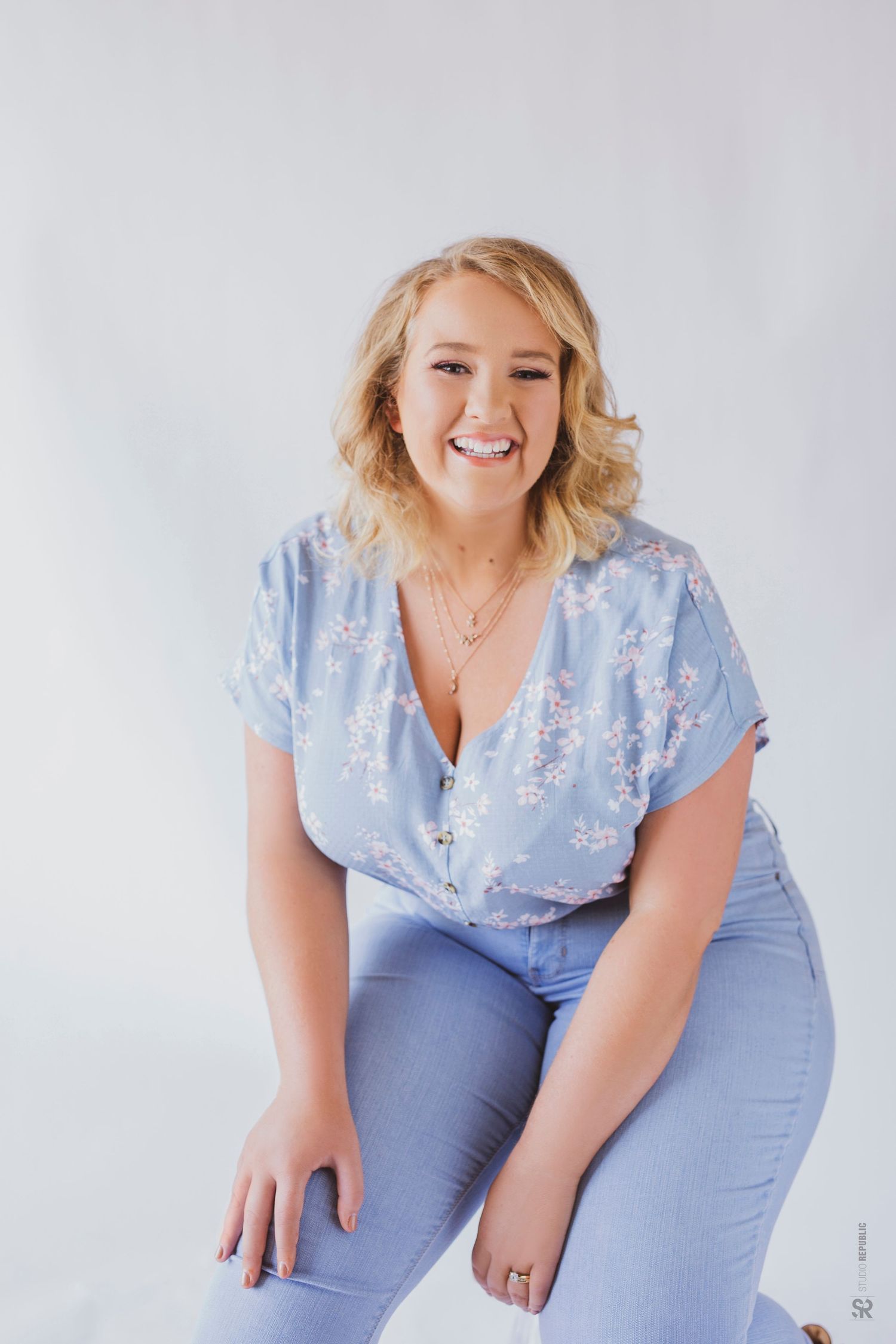 Professional studio photo of a blonde haired woman wearing blue shirt and jeans smiling