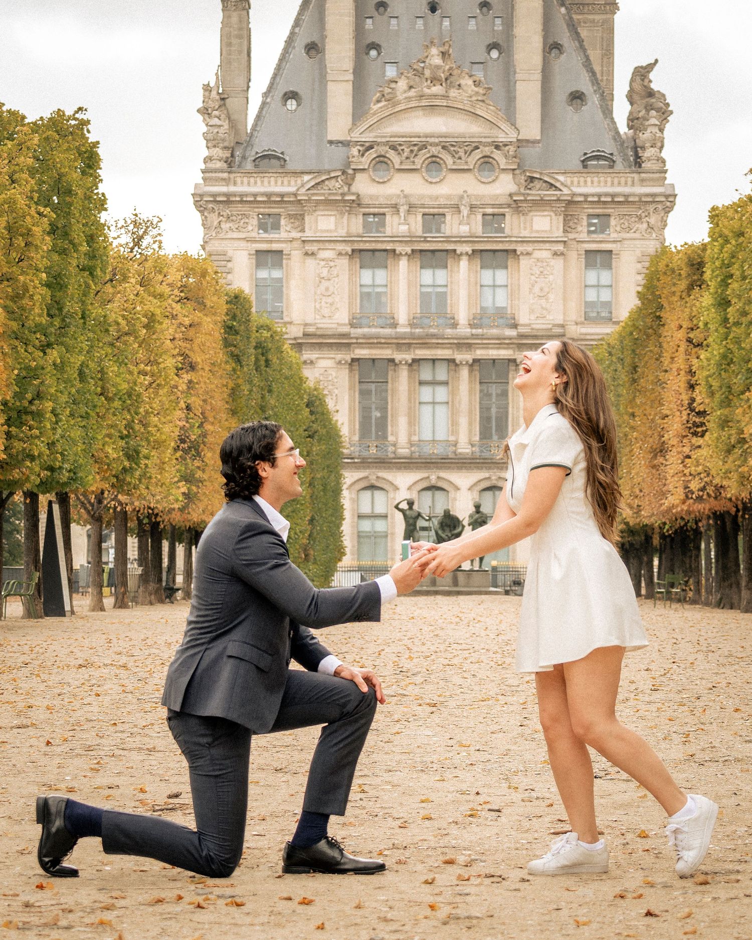 Man proposing on one knee to a woman in a white dress at the Tuileries Garden in Paris, France.