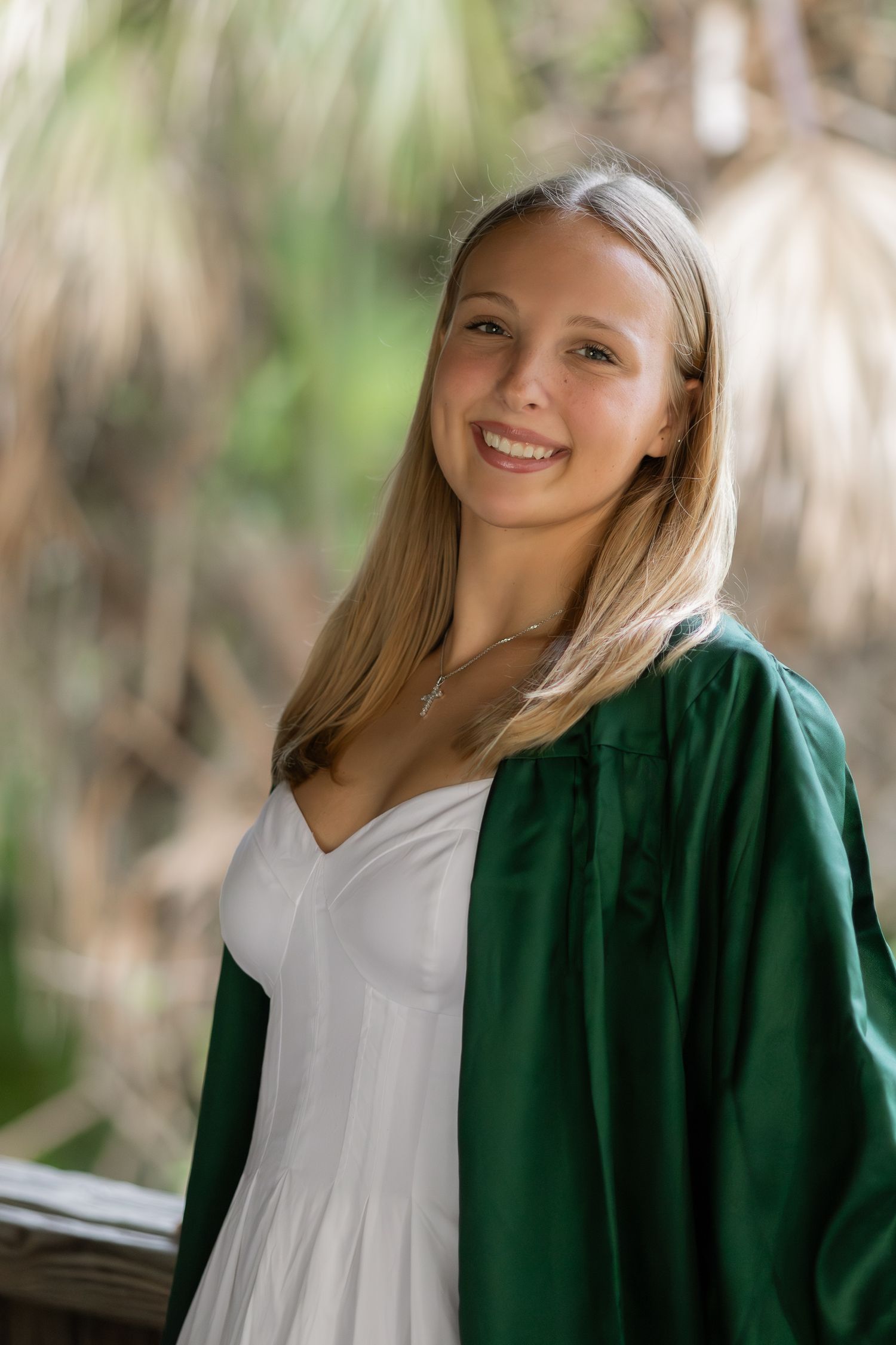 Outdoor portrait of a young woman wearing a green graduation gown