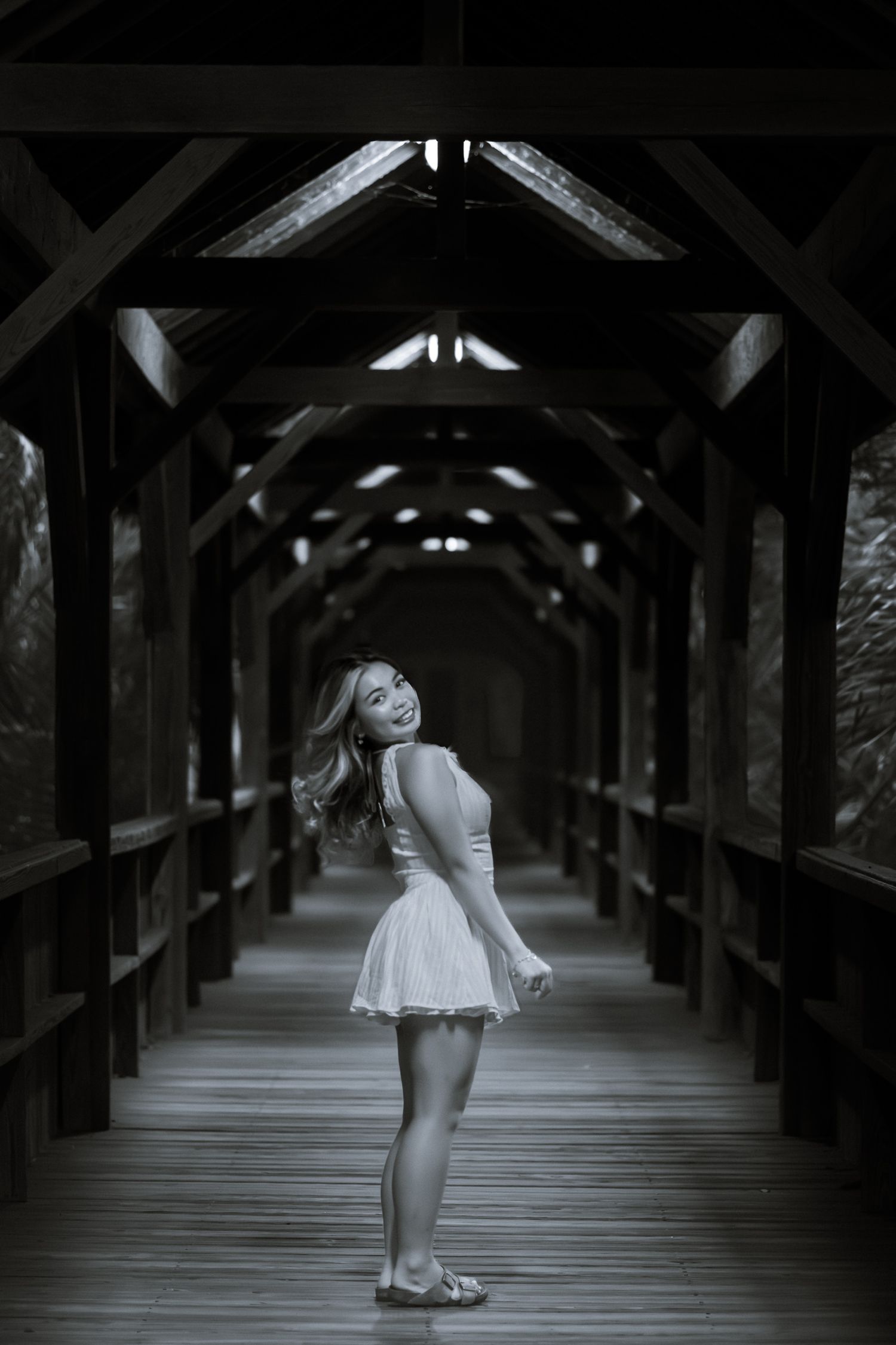 Black and white photo of a young woman in the center of the wooden bridge.