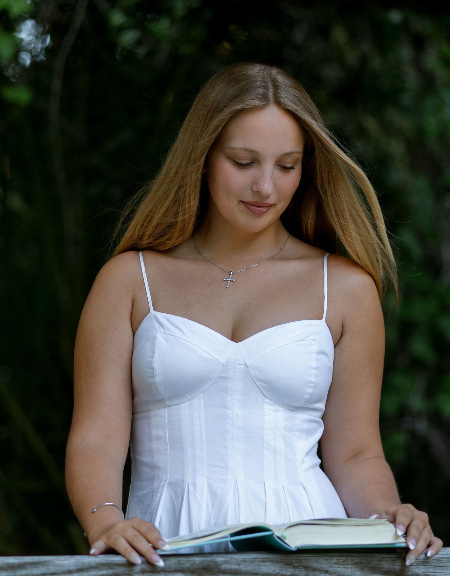 Young woman in a white dress reading a book outdoors