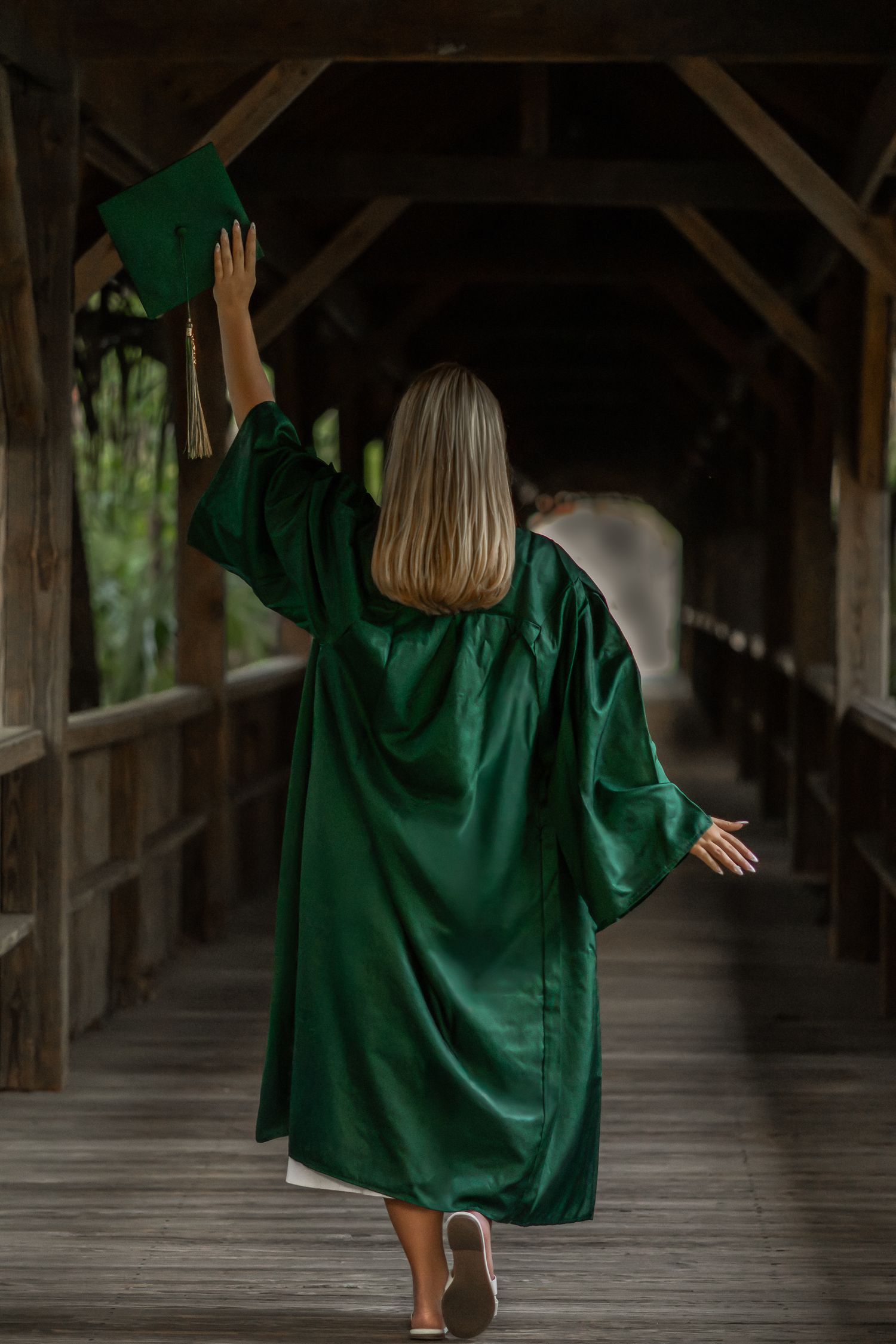 Young woman in a green graduation gown walking along a covered walkway