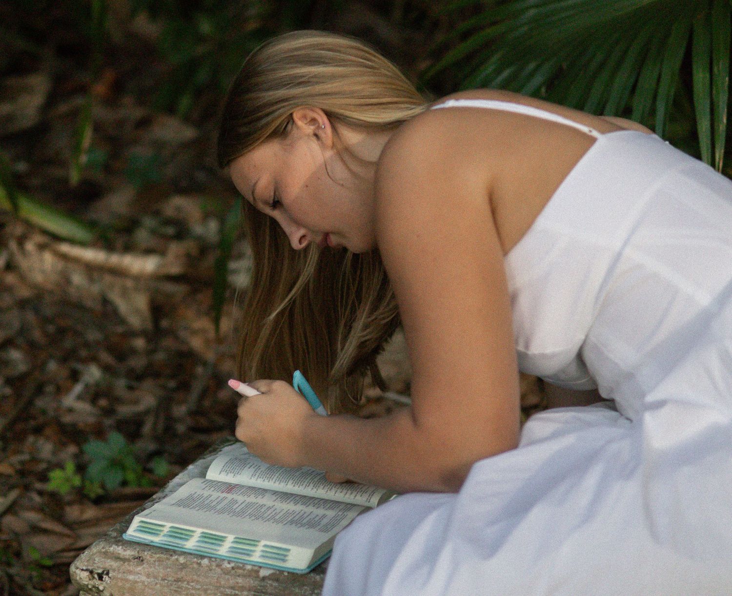 Young woman in a white dress looking through a book outdoors
