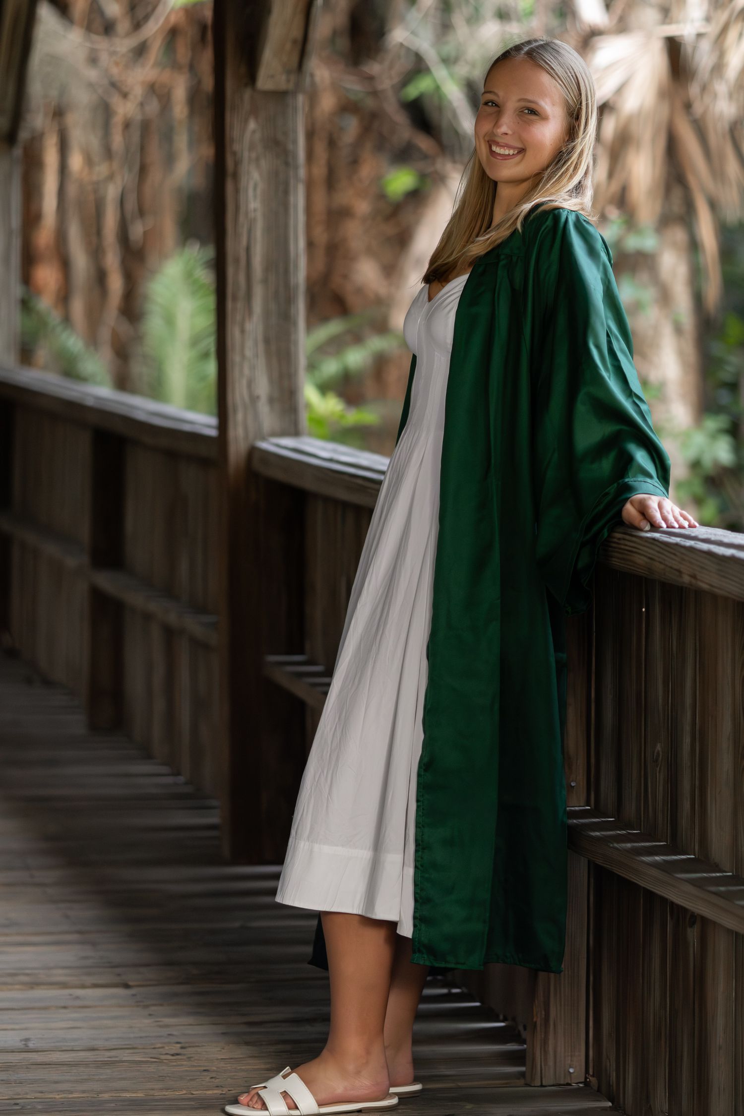 Young woman in a green graduation gown posing by a wooden railing