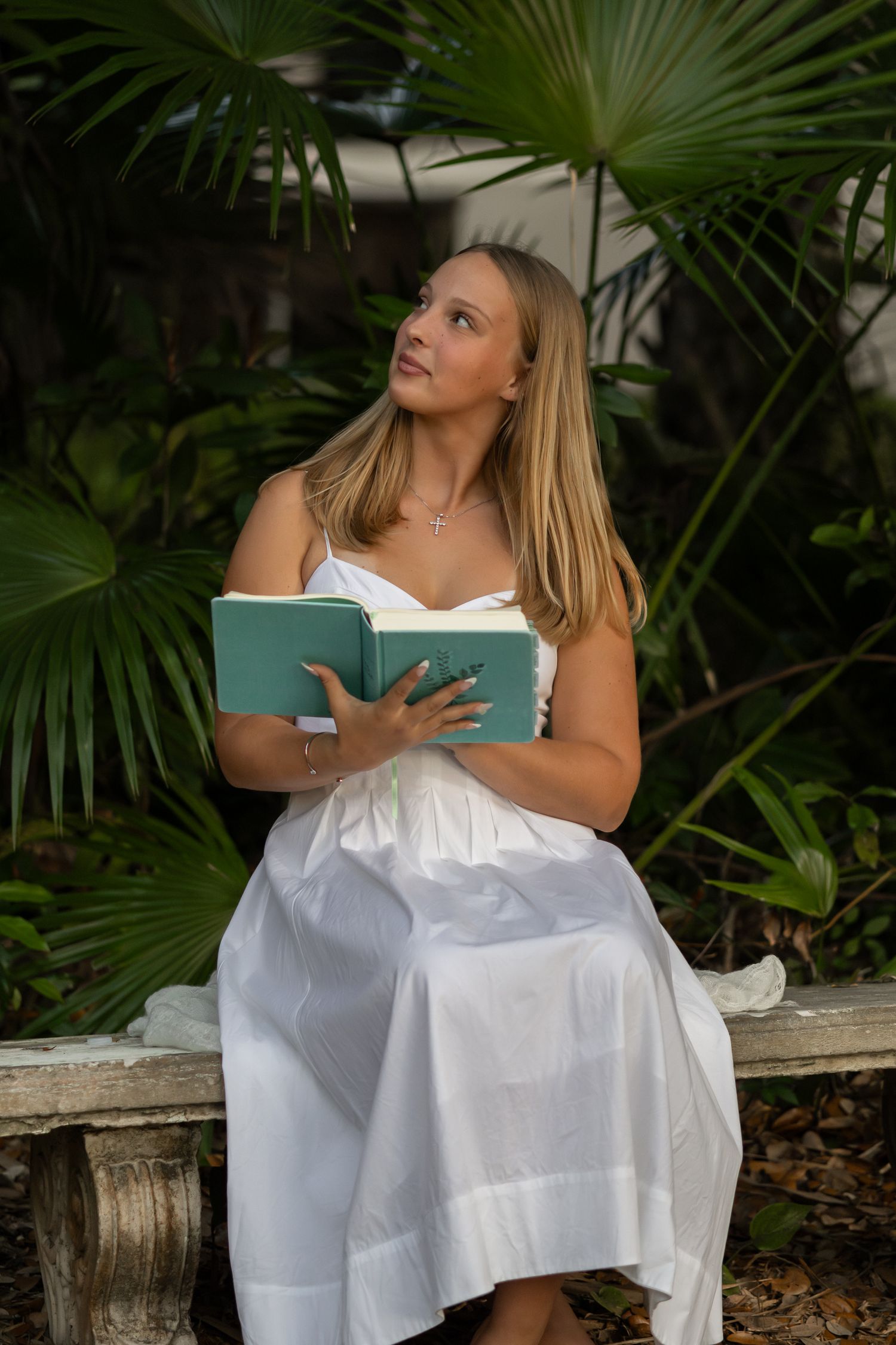 Young woman in a white dress reading a book outdoors