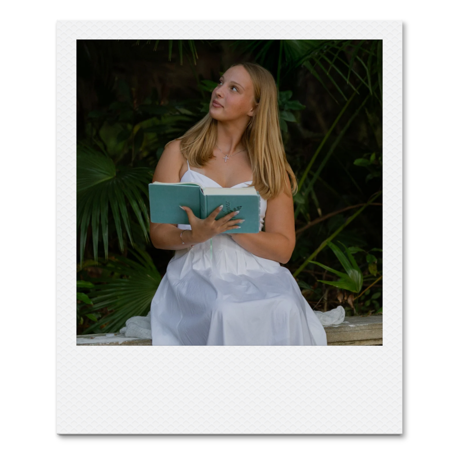 Young woman in a white dress reading a book outdoors