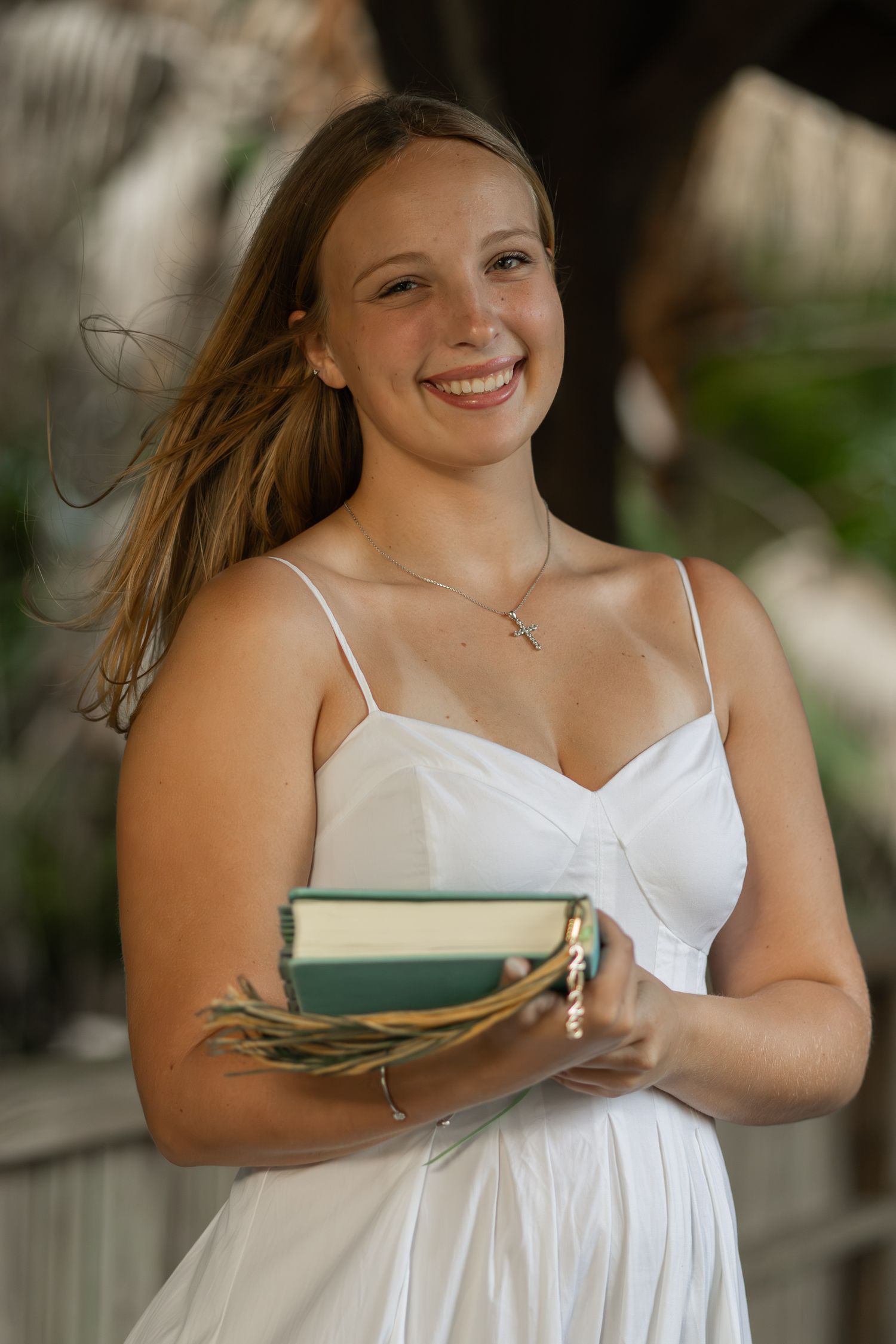 Outdoor portrait of a young woman in a white dress holding a book
