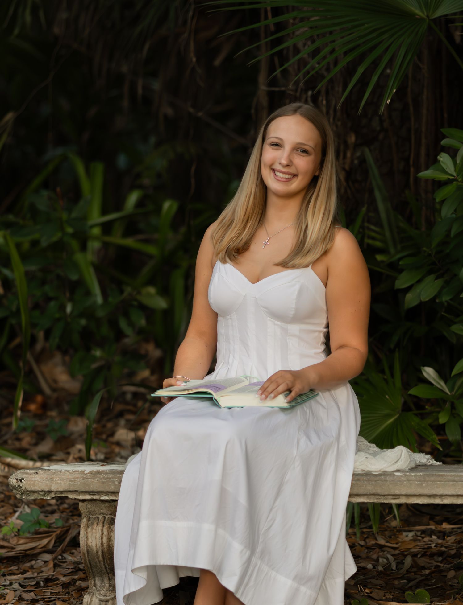 Young woman in a white dress reading a book outdoors