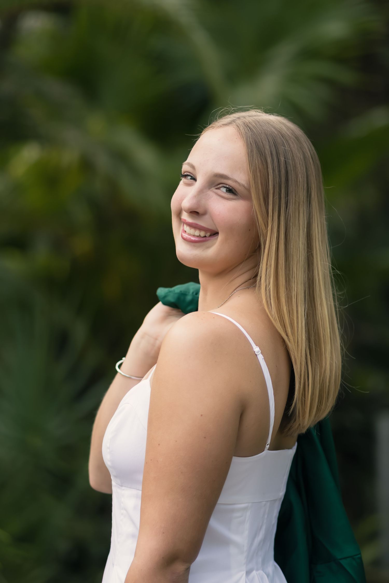 Young woman in a green graduation gown looking over her shoulder