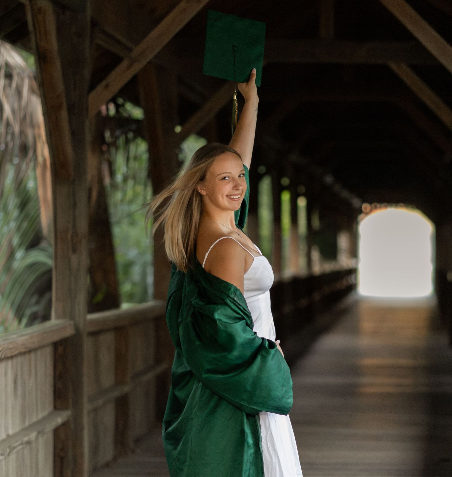 Young woman in a green graduation gown posing beside a wooden railing