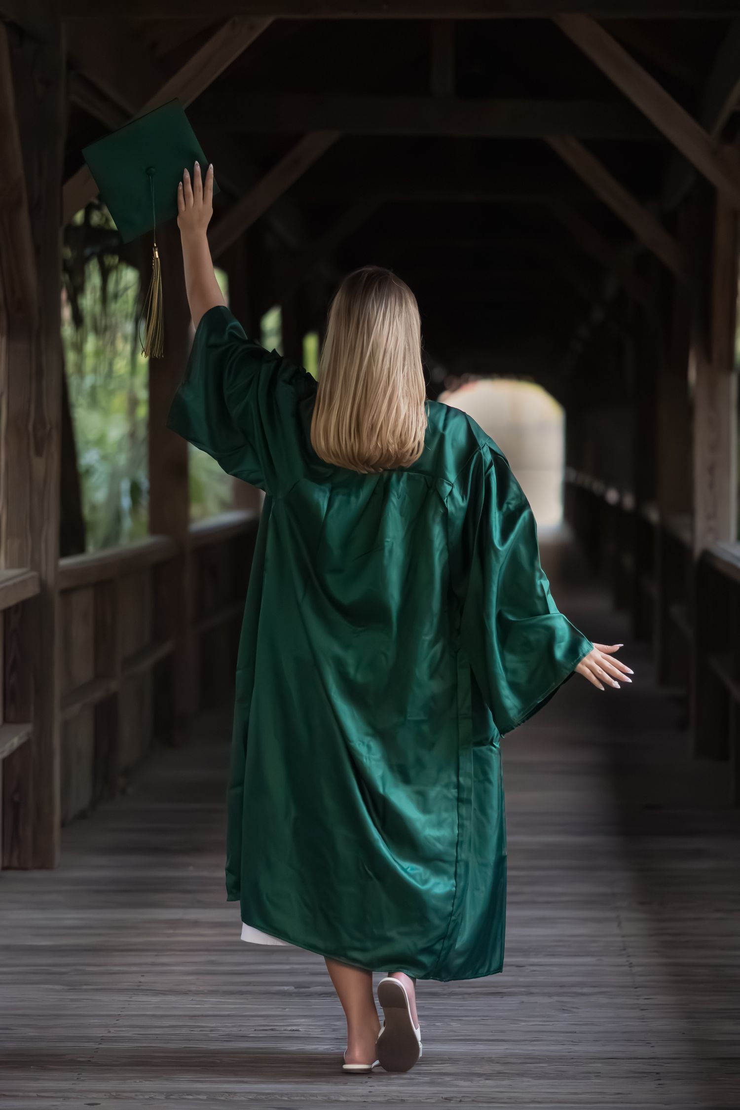 Young woman in a green graduation gown walking along a covered walkway