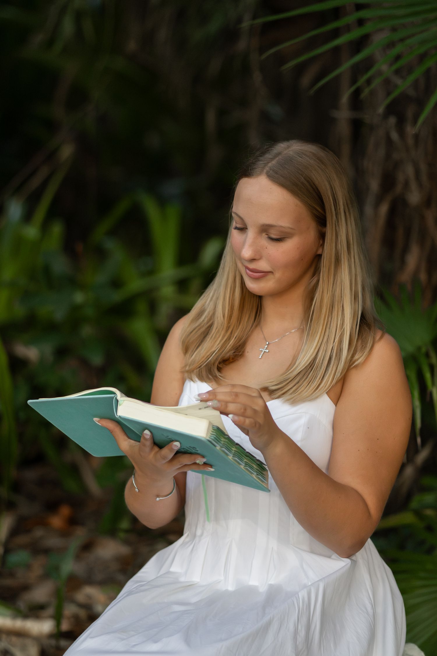 Young woman in a white dress reading a book outdoors