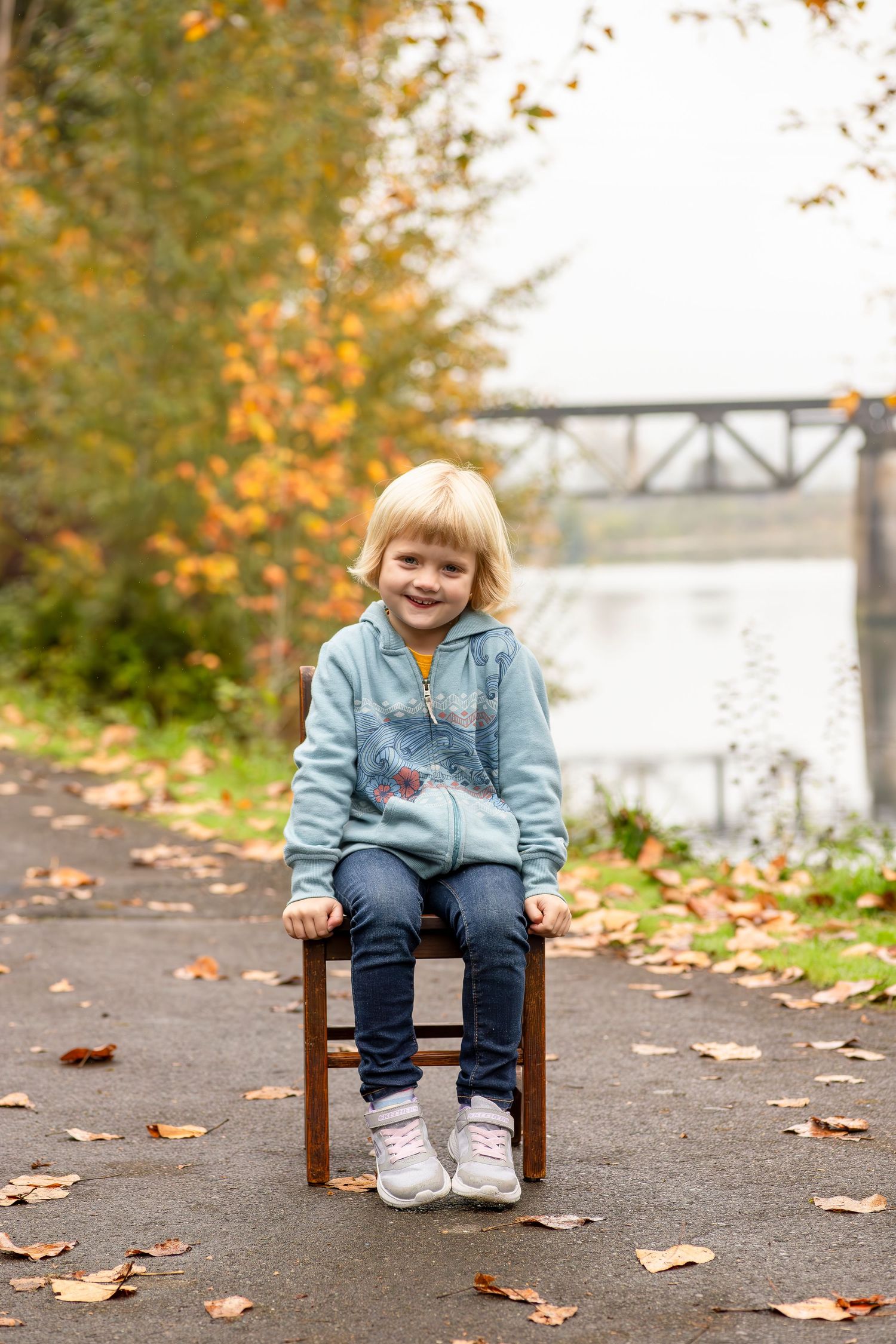 A sequence of candid moments captured outdoors on a wooden chair surrounded by autumn leaves and a bridge in the background.