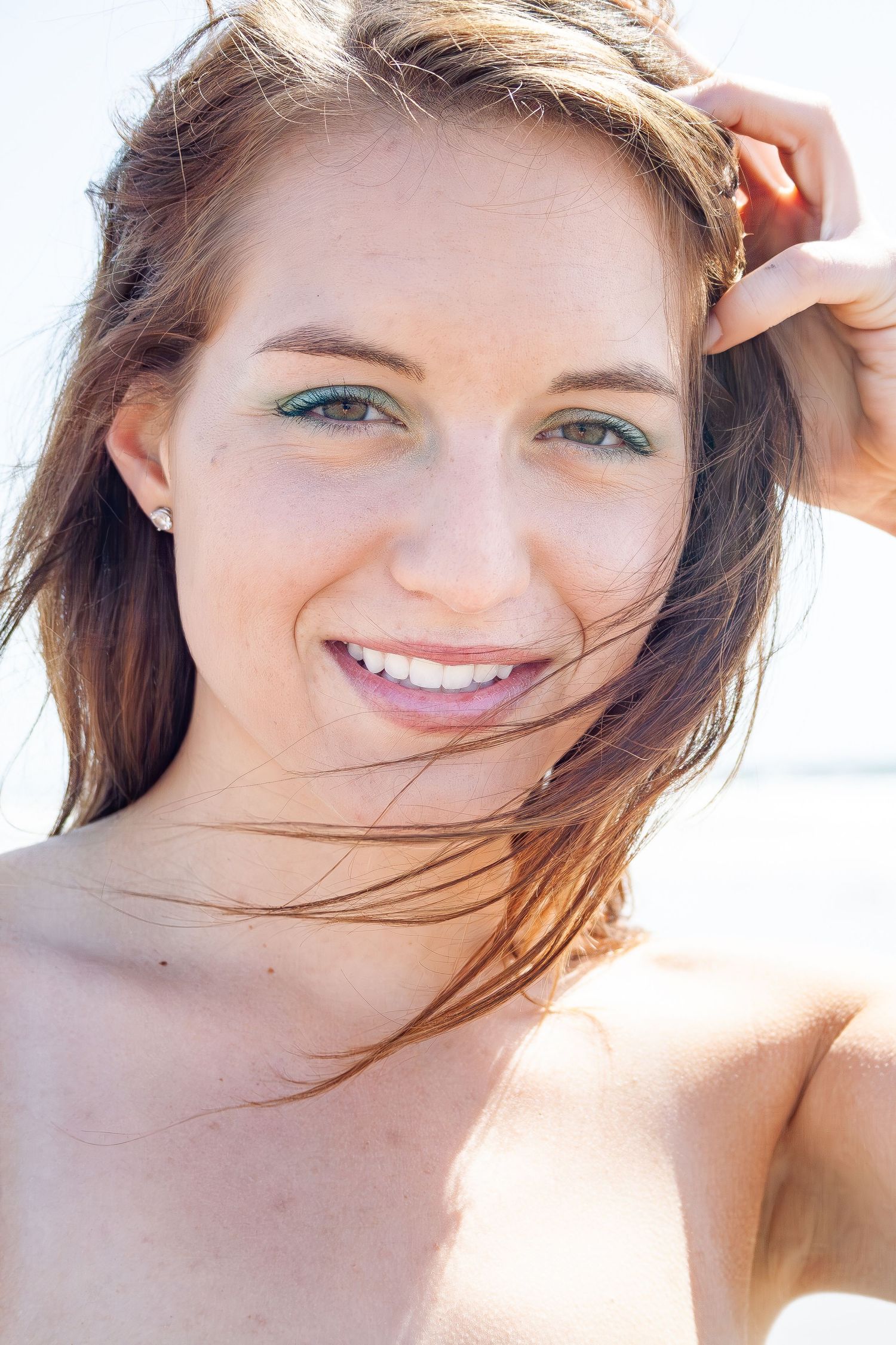 Close up outdoor portrait of a smiling person with windswept brown hair on a sunny day.
