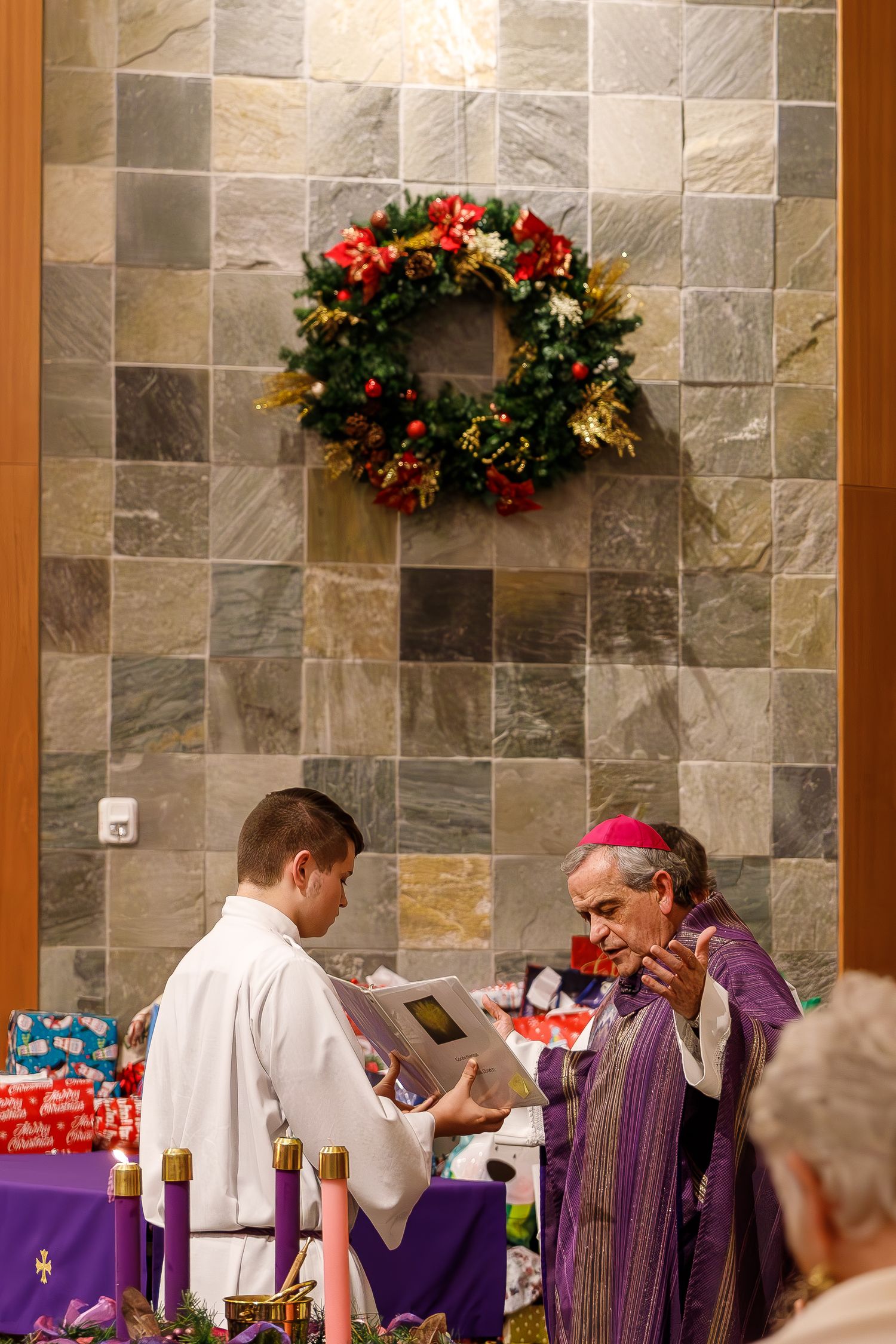 A church service during Advent with a festive wreath hanging on a stone wall above people participating in communion.