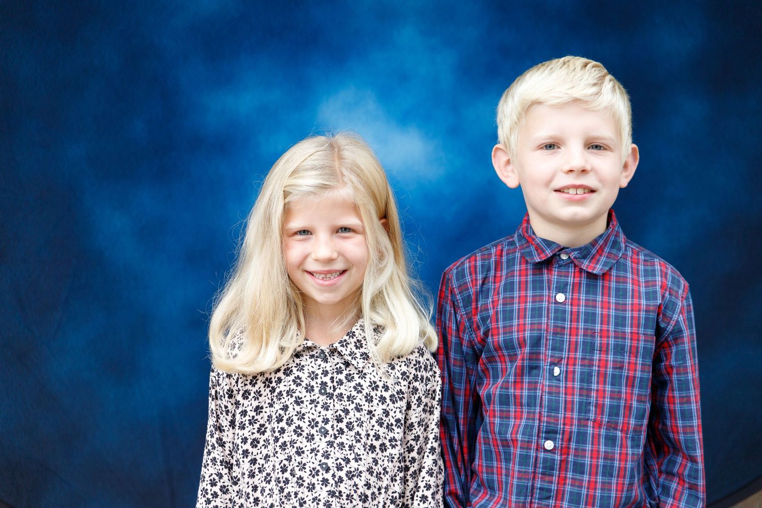 Two children pose together against a blue background wearing a plaid button down shirt and leopard print top.