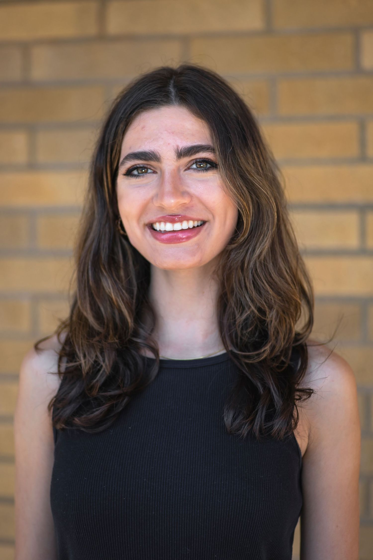 A sequence of headshots showing someone with dark wavy hair and black sleeveless top smiling against a brick wall.